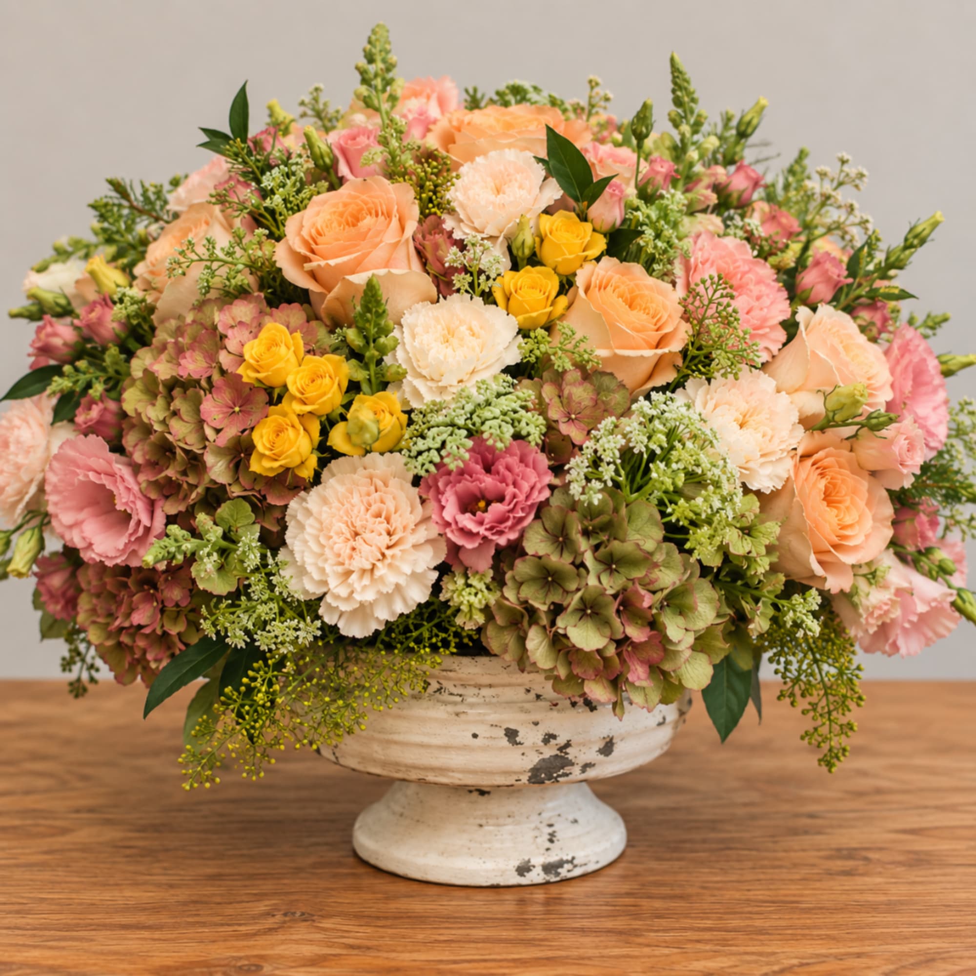 Mixed pink, peach, white, and yellow flowers in a white pedestal vase