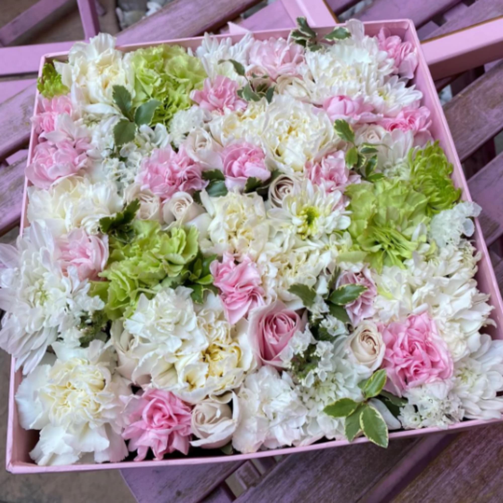 Square pink box filled with tightly packed white, pink, and green flowers in a flat arrangement