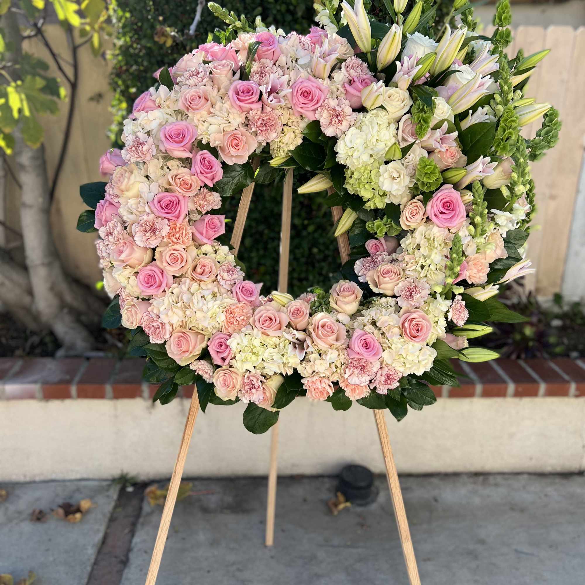 Large standing wreath of pink roses, carnations, and white hydrangeas on a wooden easel