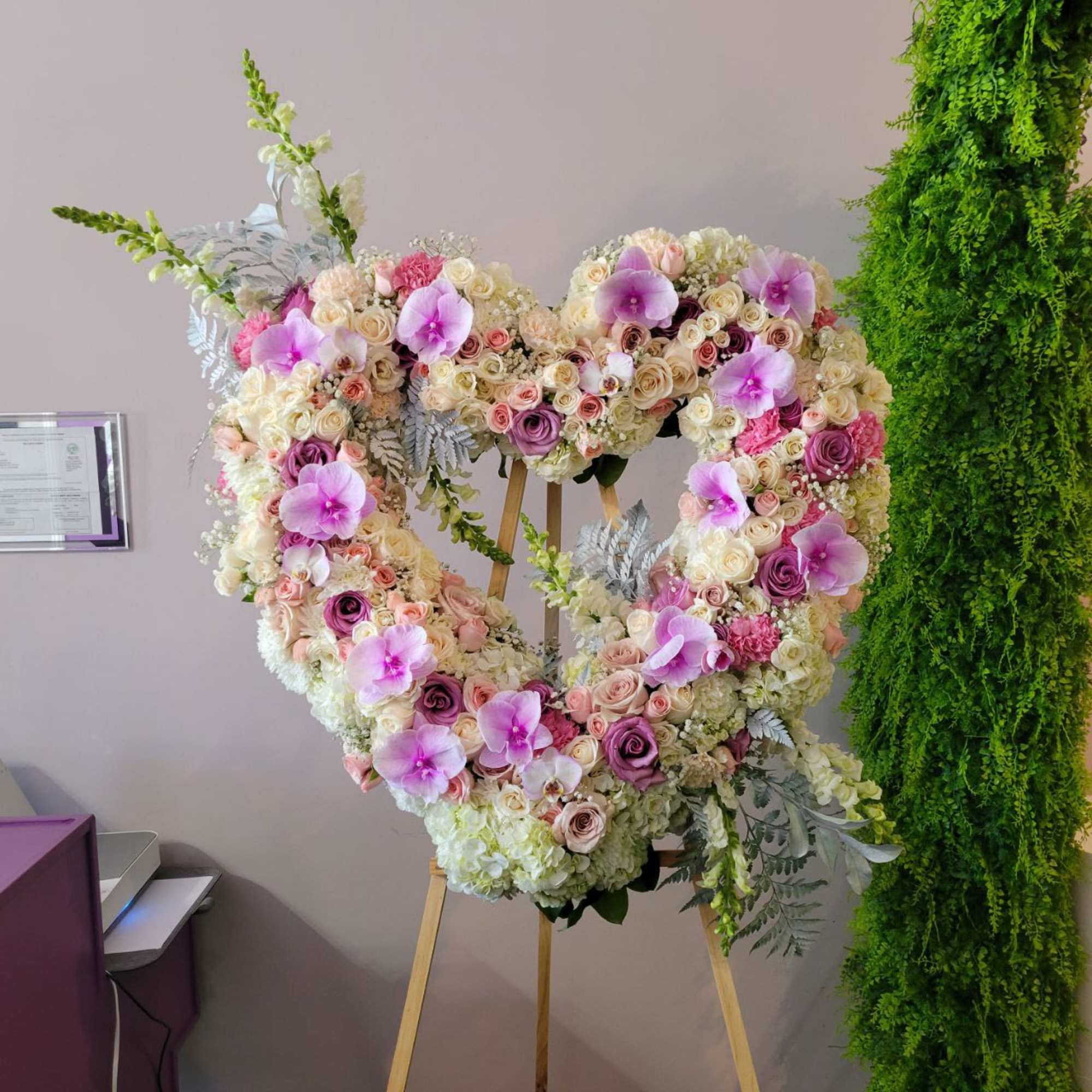 Tall heart-shaped standing wreath of pastel roses, orchids, and hydrangeas on a wooden easel.