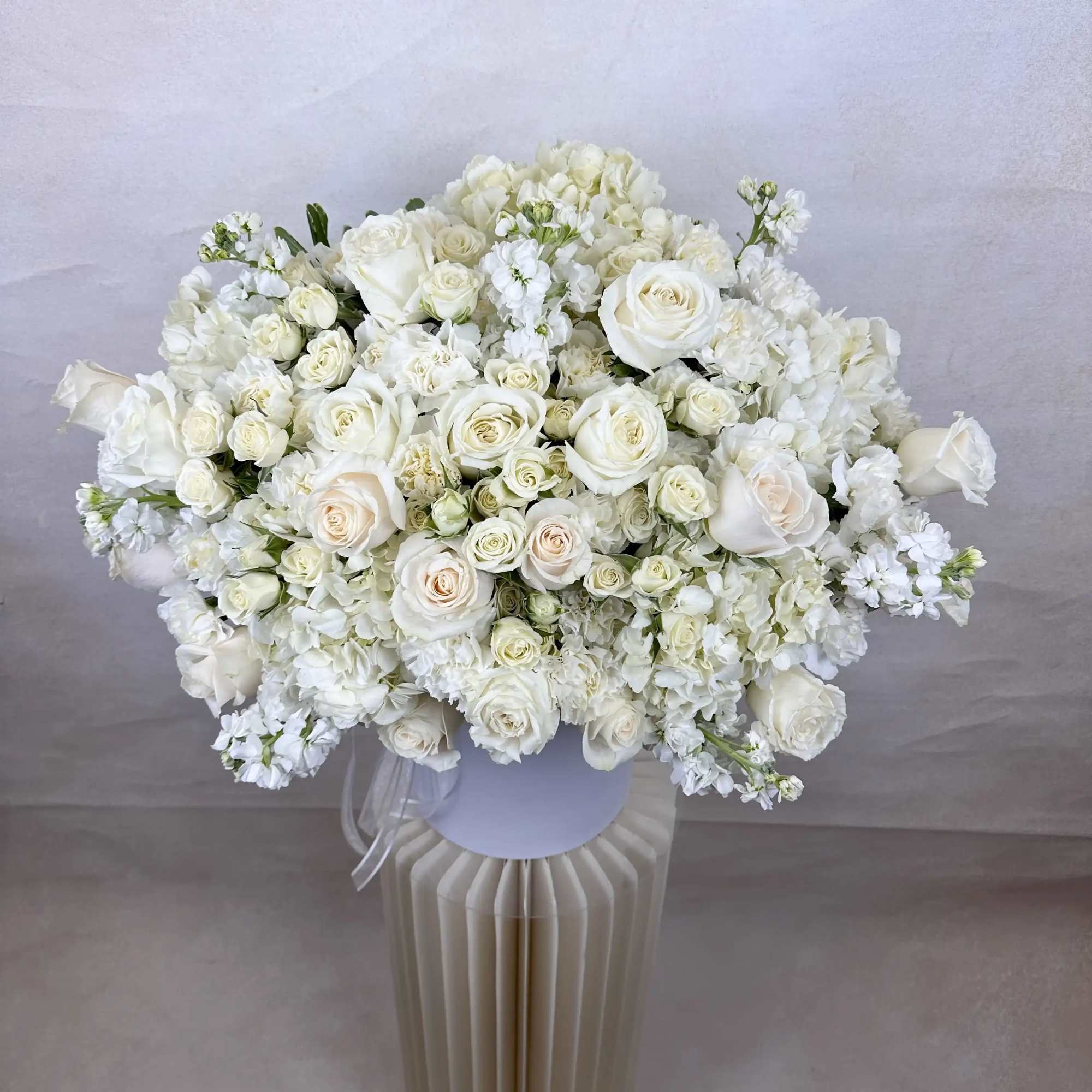 Large all-white bouquet of roses and hydrangeas in a white hatbox vase on a pedestal