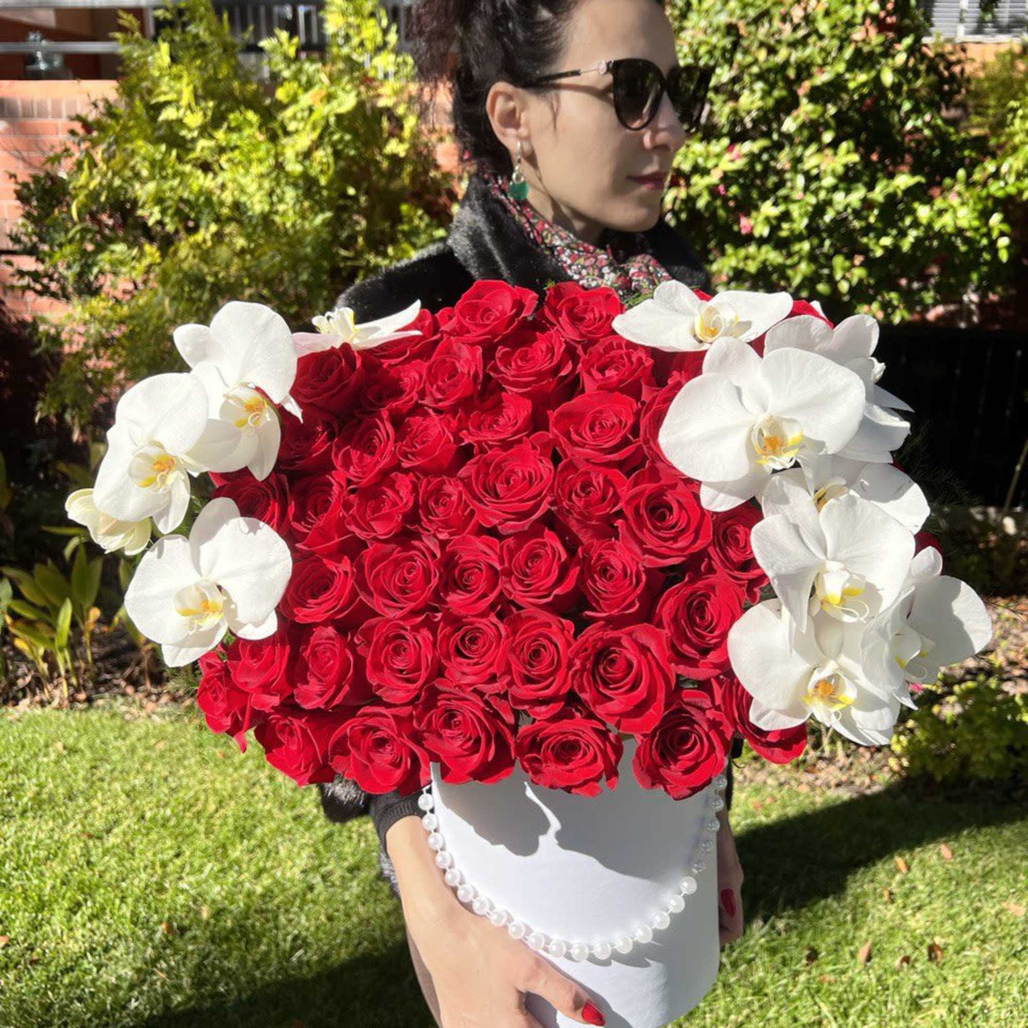 Large hatbox of red roses with white orchids held by a woman outdoors