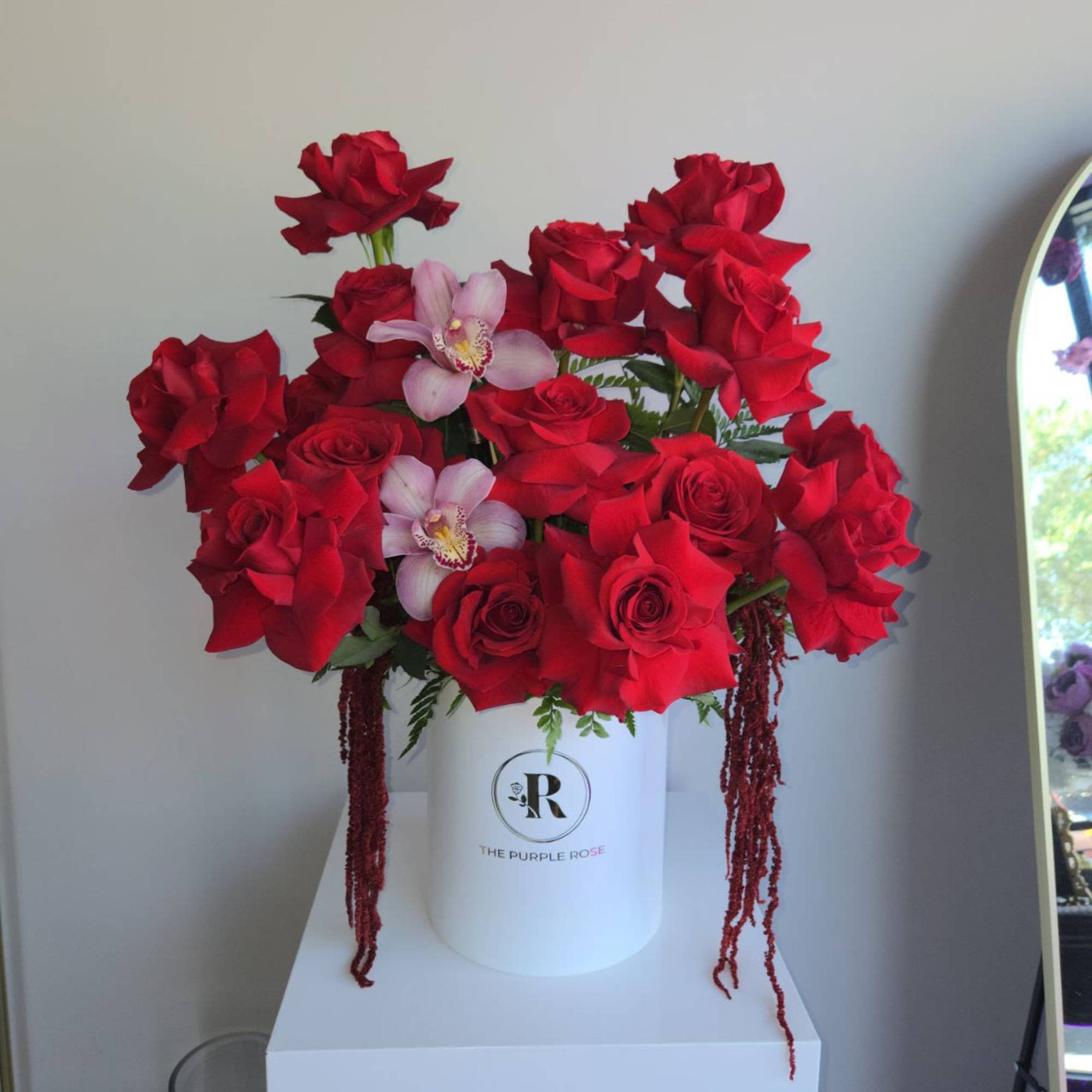 Arrangement of red roses and pink orchids in a white hatbox container