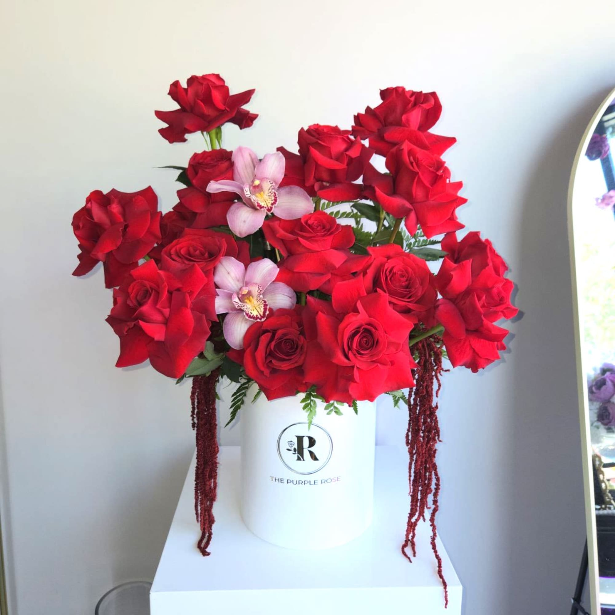 Hatbox arrangement of red roses with pink orchids in a white cylinder container