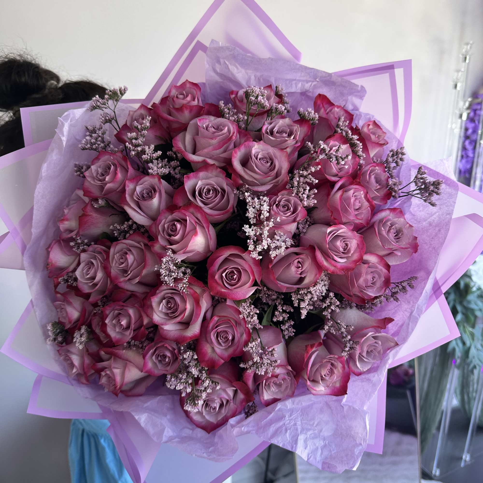 Hand-tied bouquet of mauve roses with pink edges and small filler flowers wrapped in lavender and pink paper.