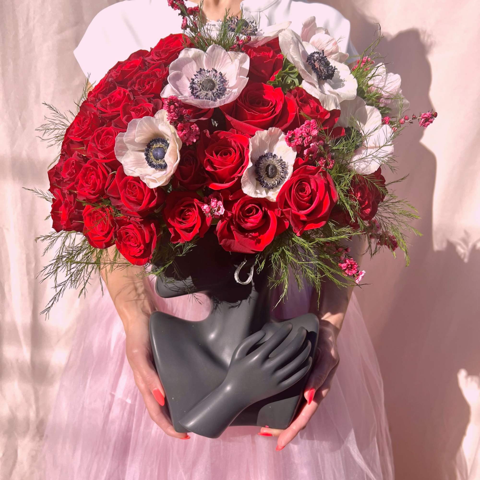 Sculptural black bust vase filled with red roses and white anemones, held in both hands.
