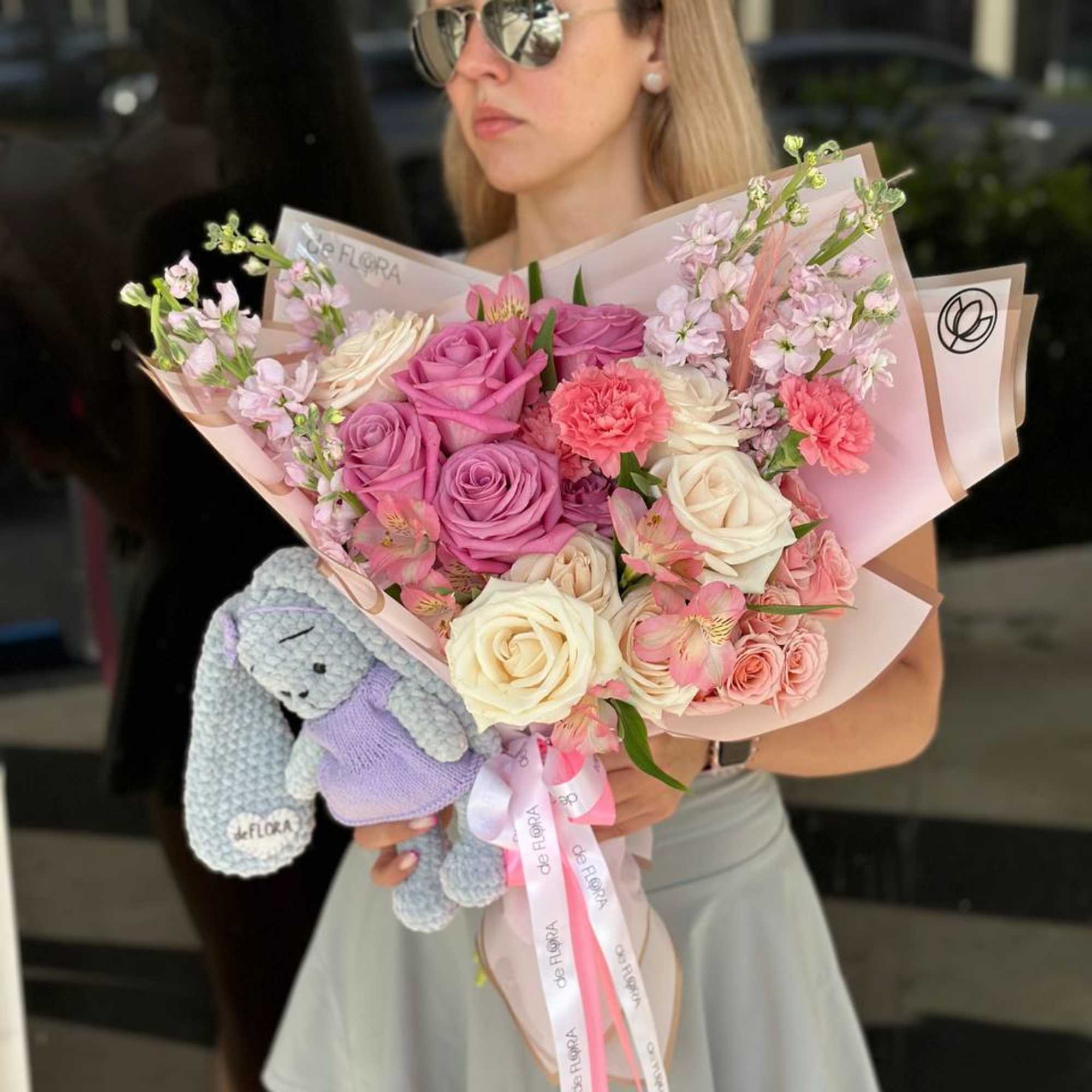 Woman holding a pastel bouquet with roses and carnations, plus a small plush bear
