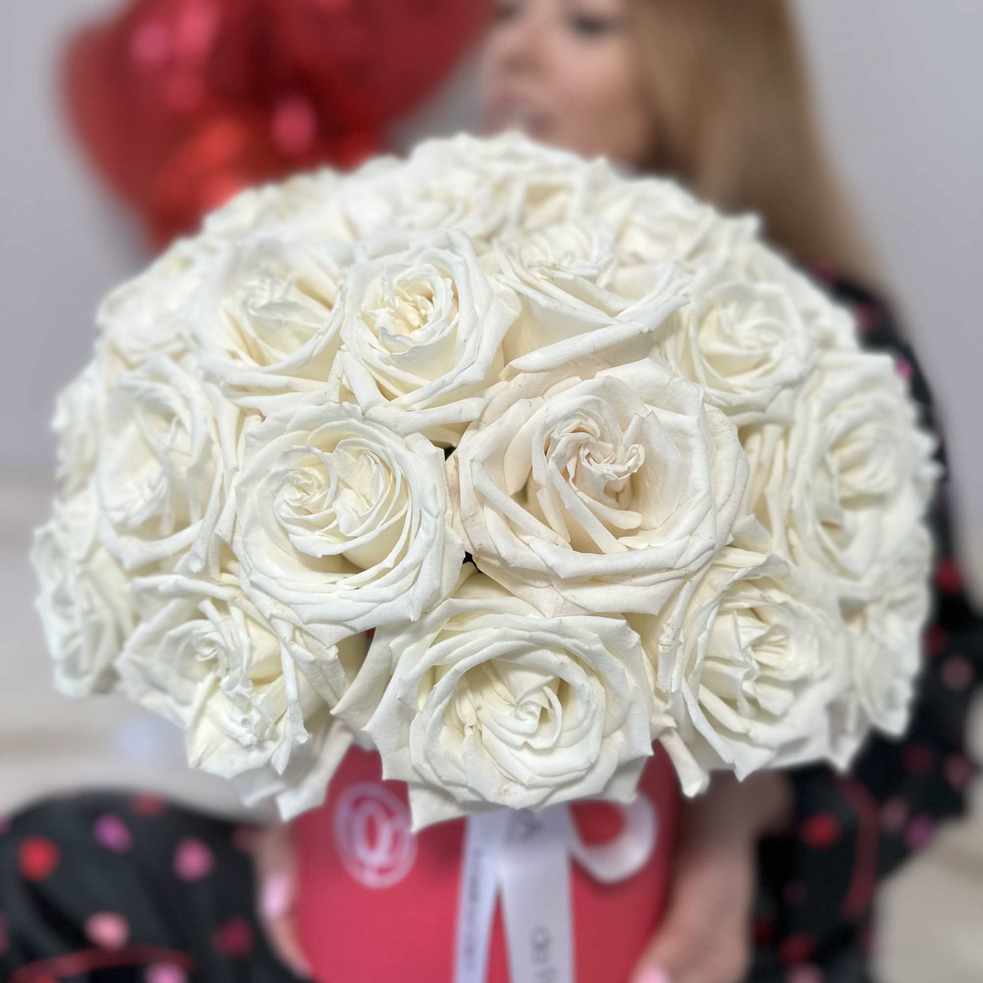 Large bouquet of white roses held in front of a person with red balloons behind