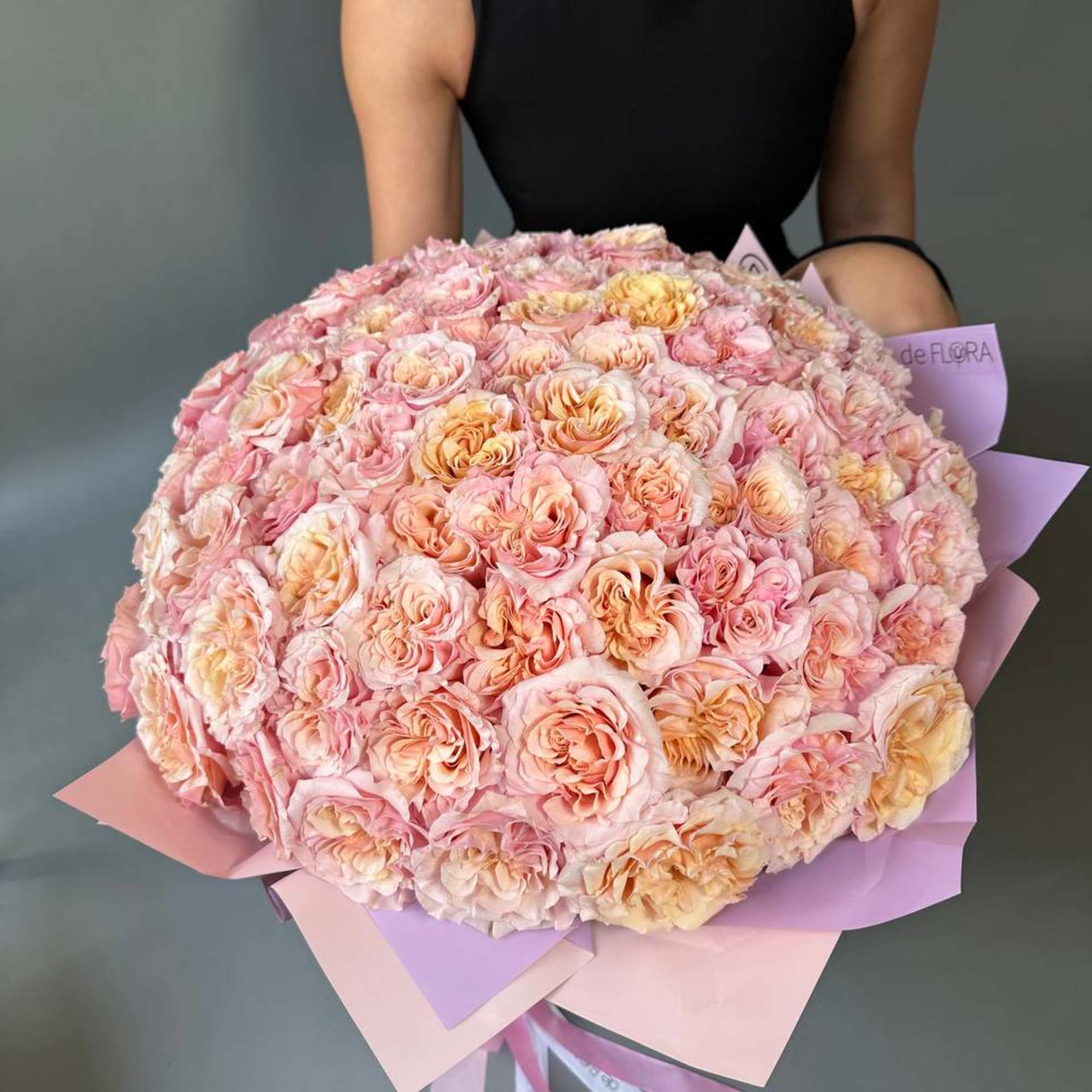 Large bouquet of pale pink and peach roses wrapped in pink and lavender paper