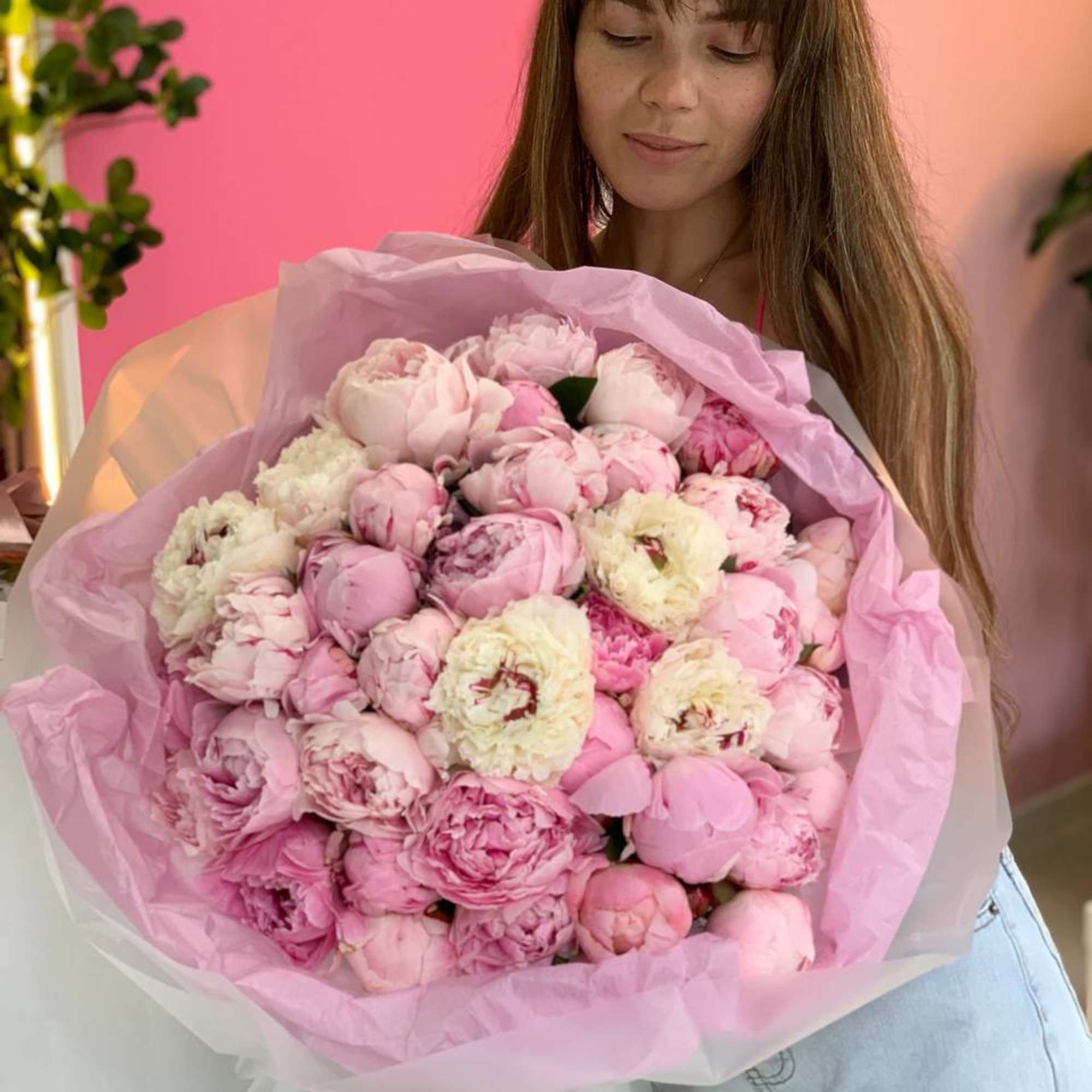 Woman holding a large bouquet of pink peonies wrapped in pink paper