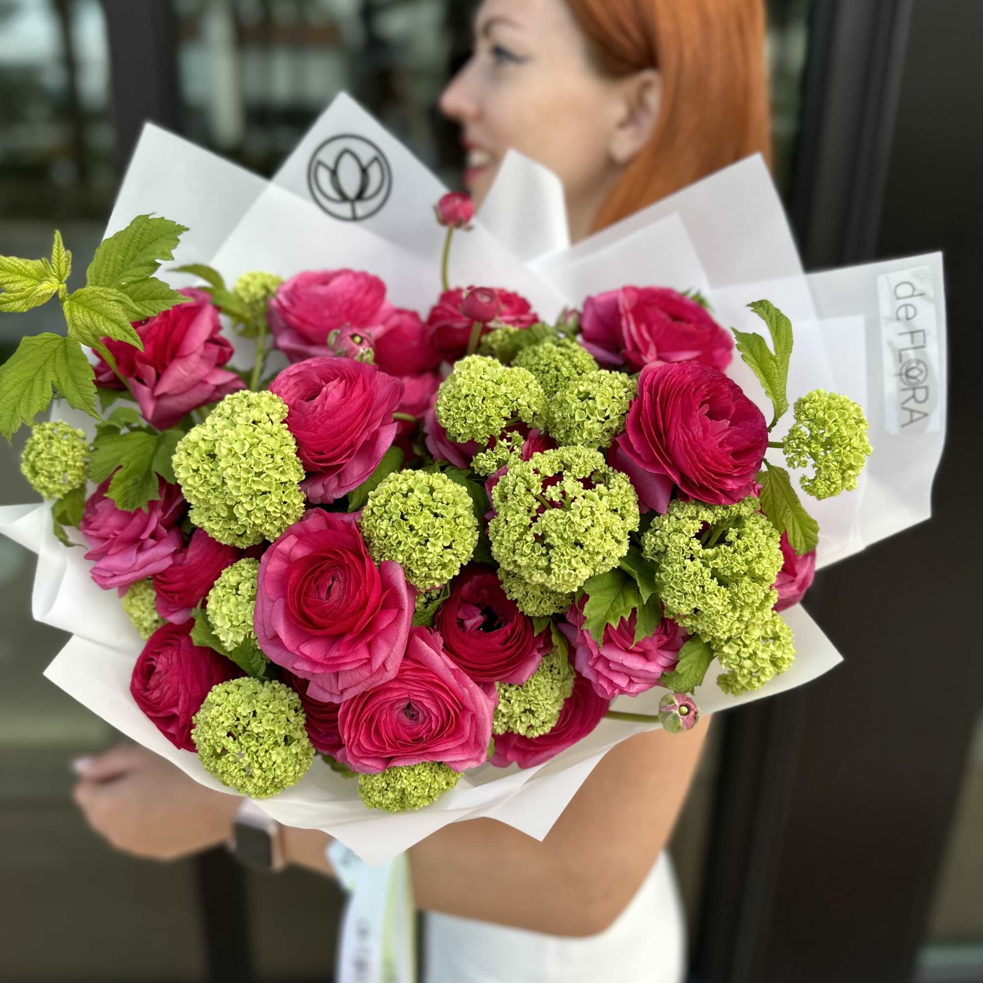 Bouquet of hot pink ranunculus and green viburnum blooms in white wrap