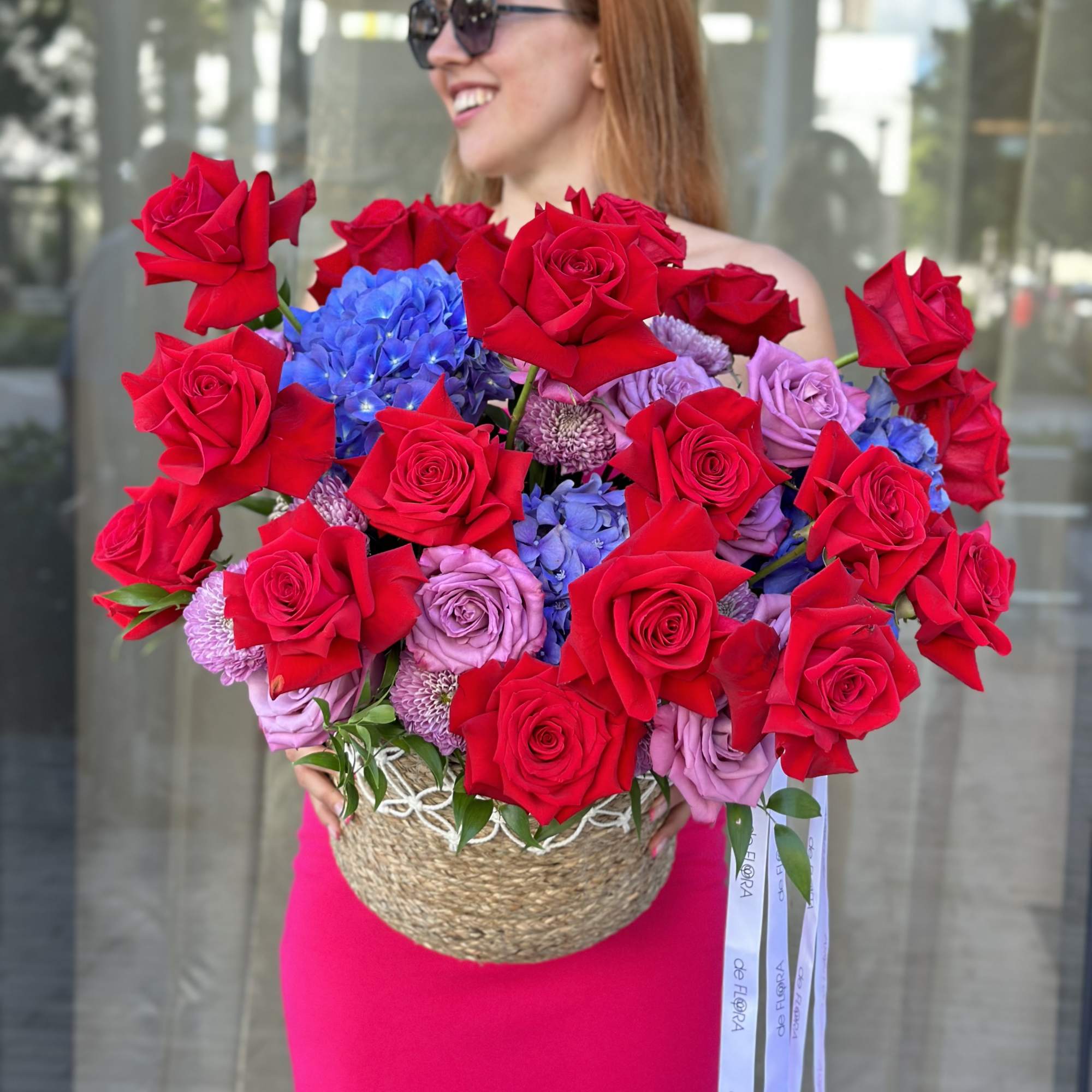 Large basket arrangement of red roses, lavender roses, and blue hydrangeas