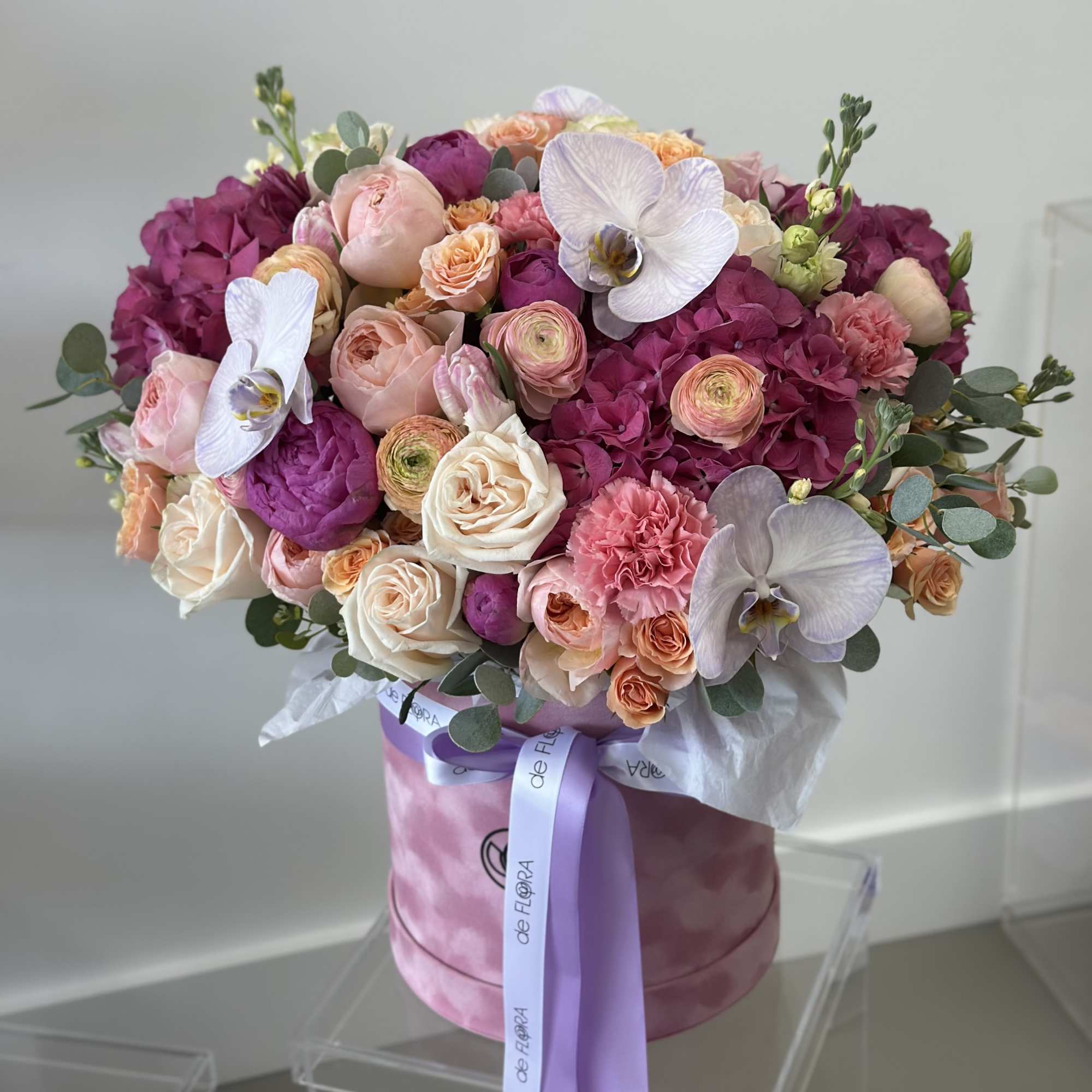 Bouquet of pink and peach roses with white orchids in a pink hatbox