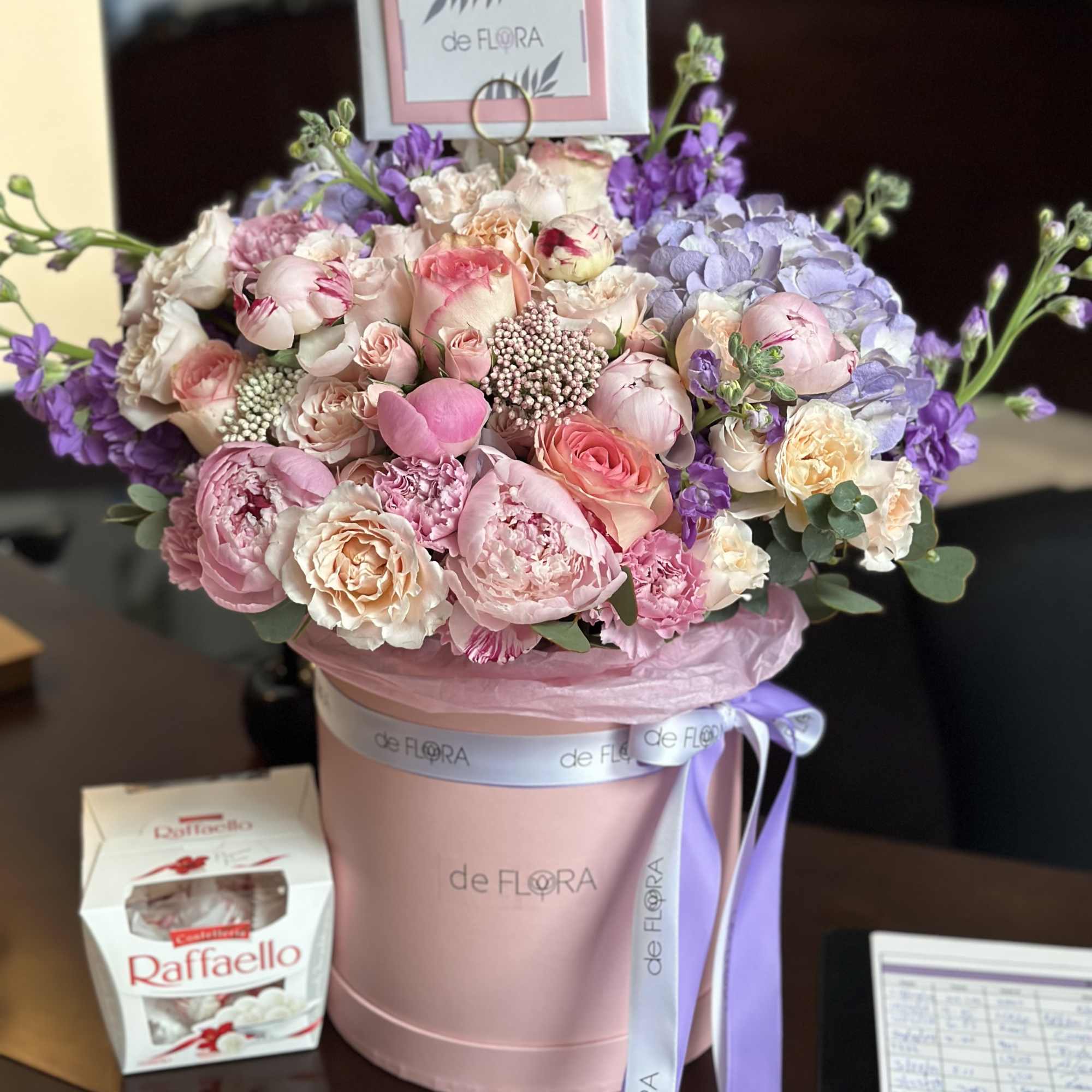 Pink and lavender flower arrangement in a round box with a ribbon.