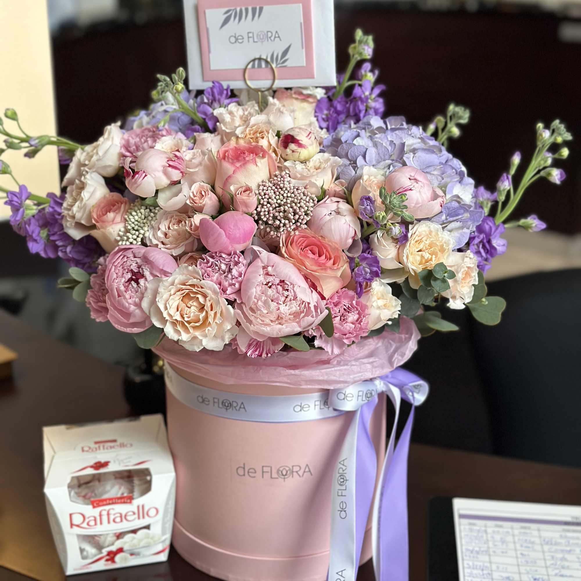 Pink and lavender bouquet in a round hatbox with a ribbon and candy box
