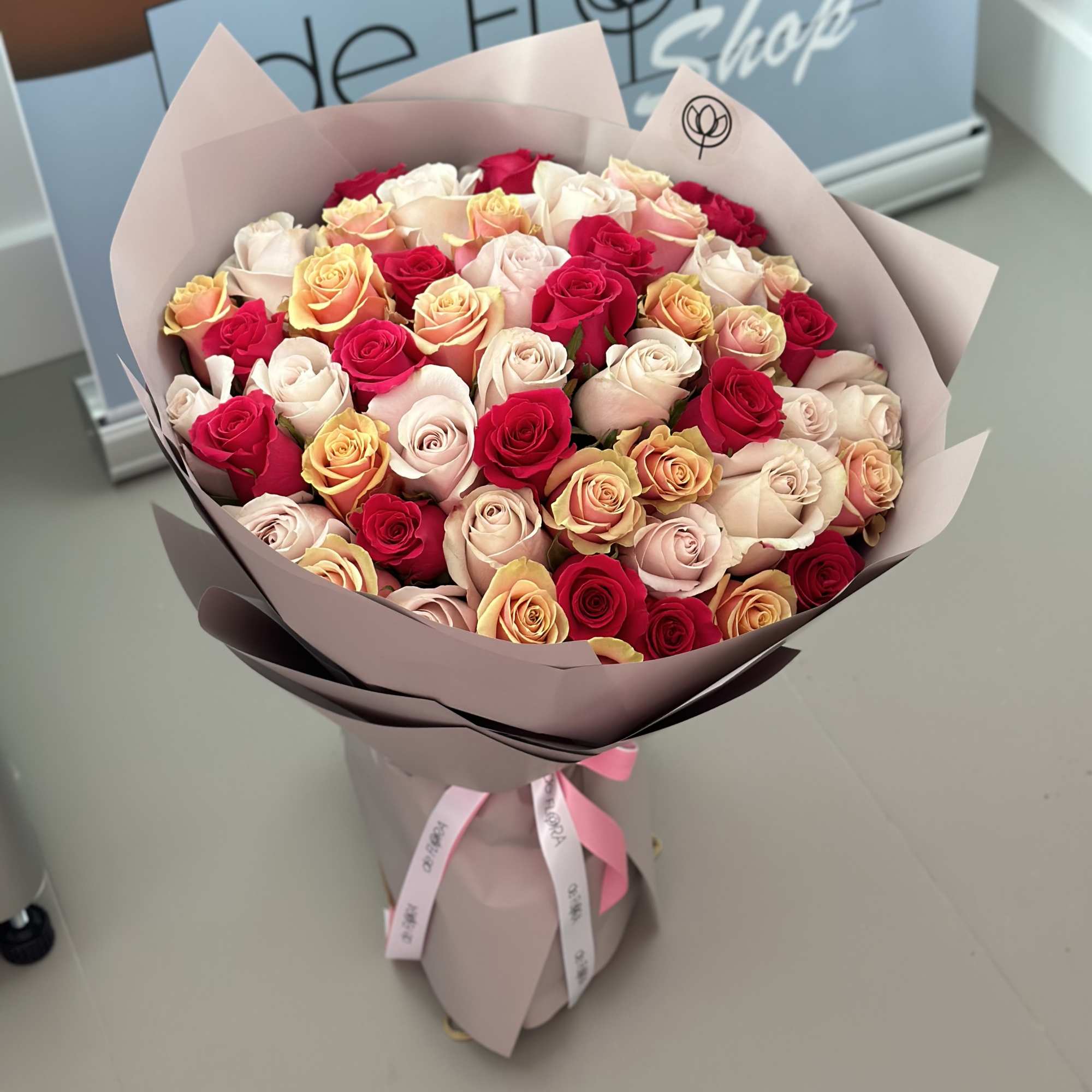 Bouquet of red, blush, and peach roses wrapped in pale pink paper