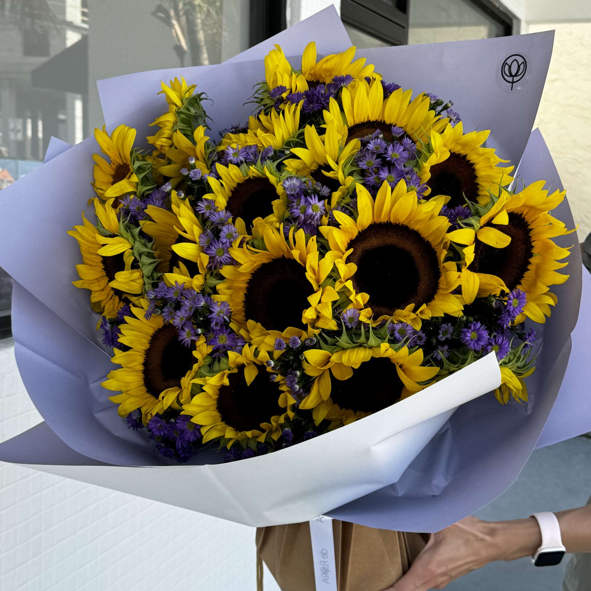 Bouquet of sunflowers and purple daisies wrapped in lavender paper