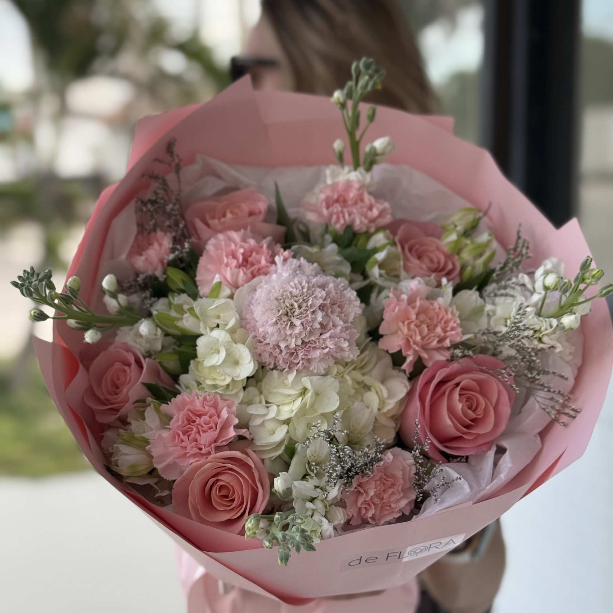 Pink bouquet of roses, carnations, and white hydrangeas wrapped in pink paper