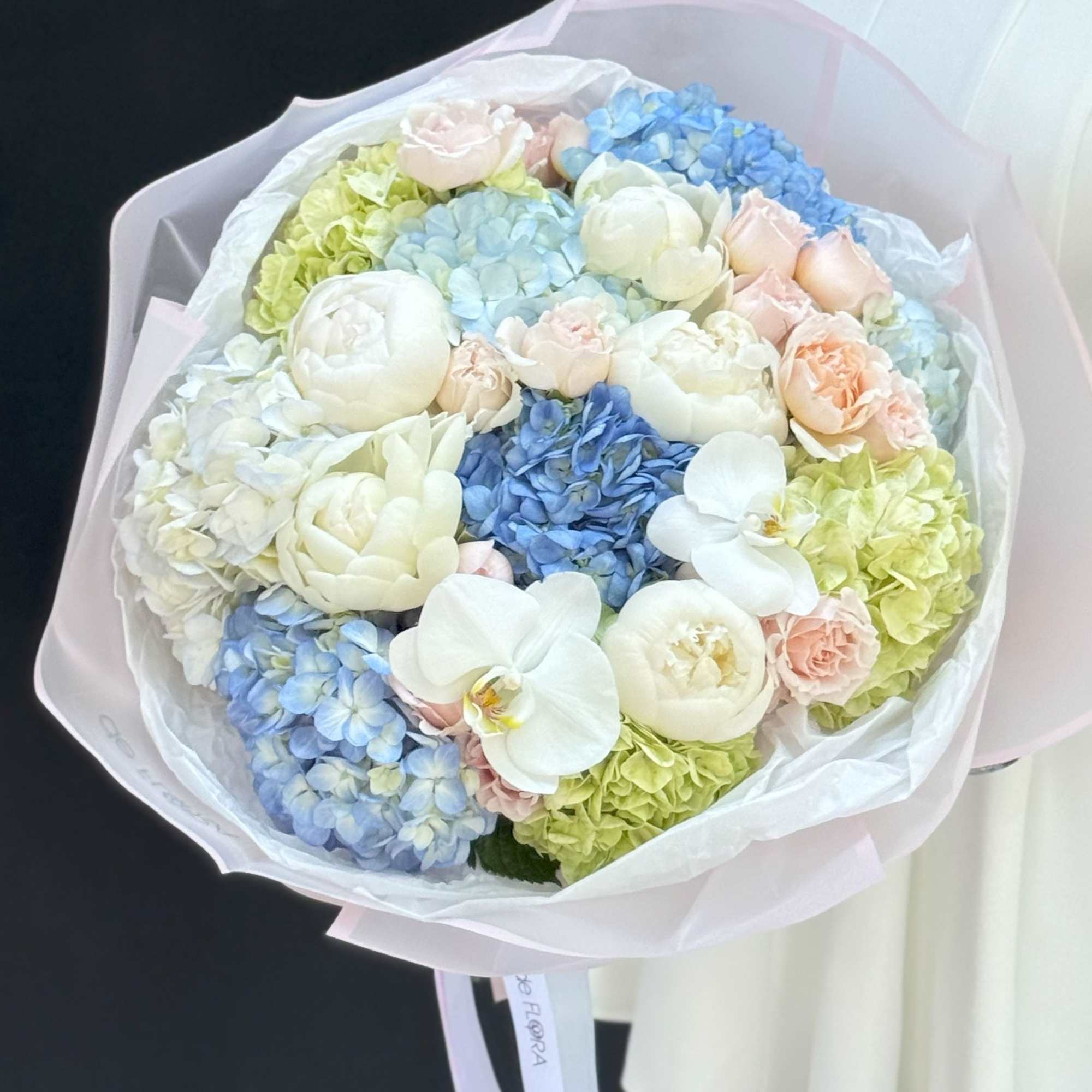 Pastel bouquet of hydrangeas, roses, and white orchids wrapped in pink paper