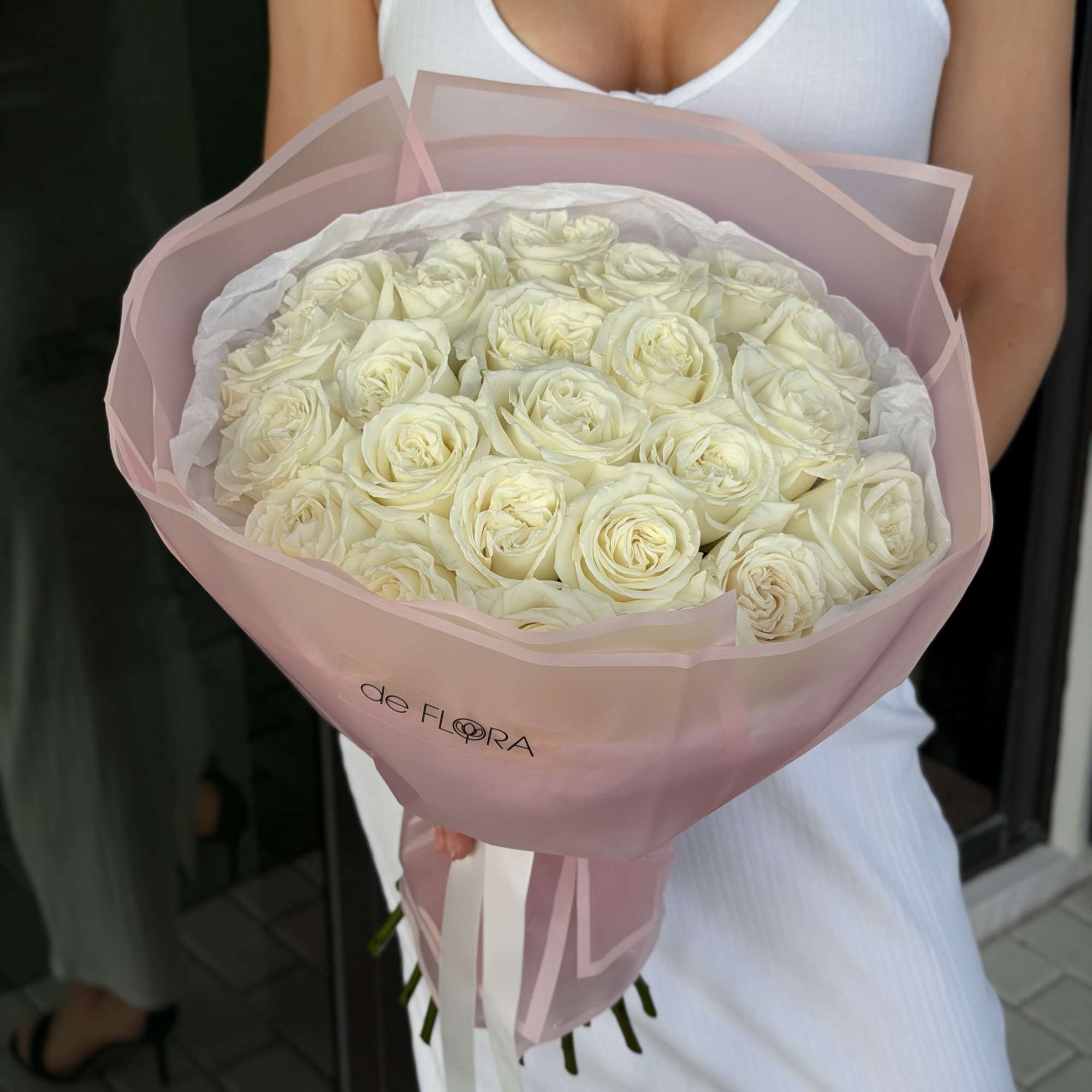 Large bouquet of cream roses wrapped in pink paper, held by a person in a white dress