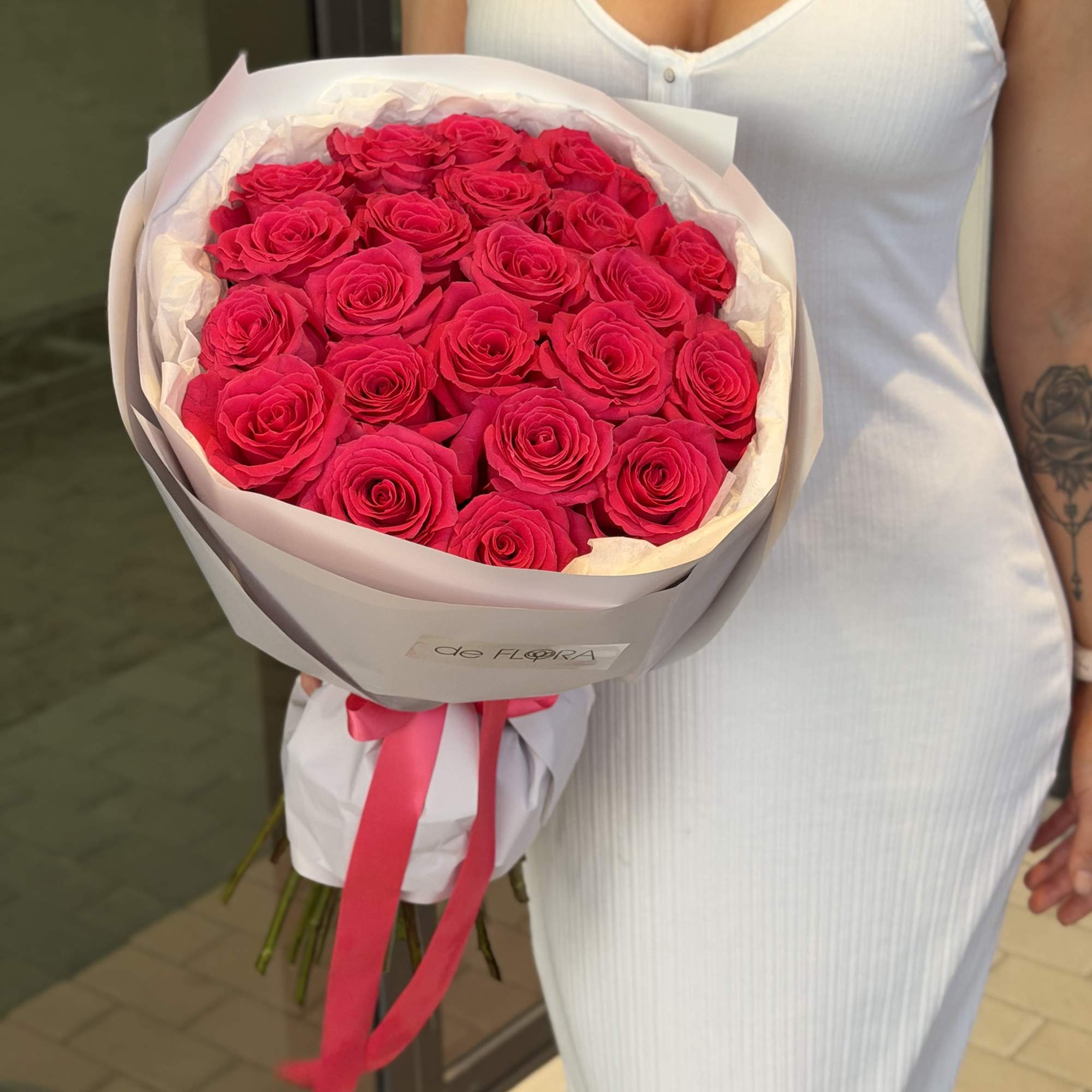 Large bouquet of bright pink roses wrapped in white paper with a pink ribbon