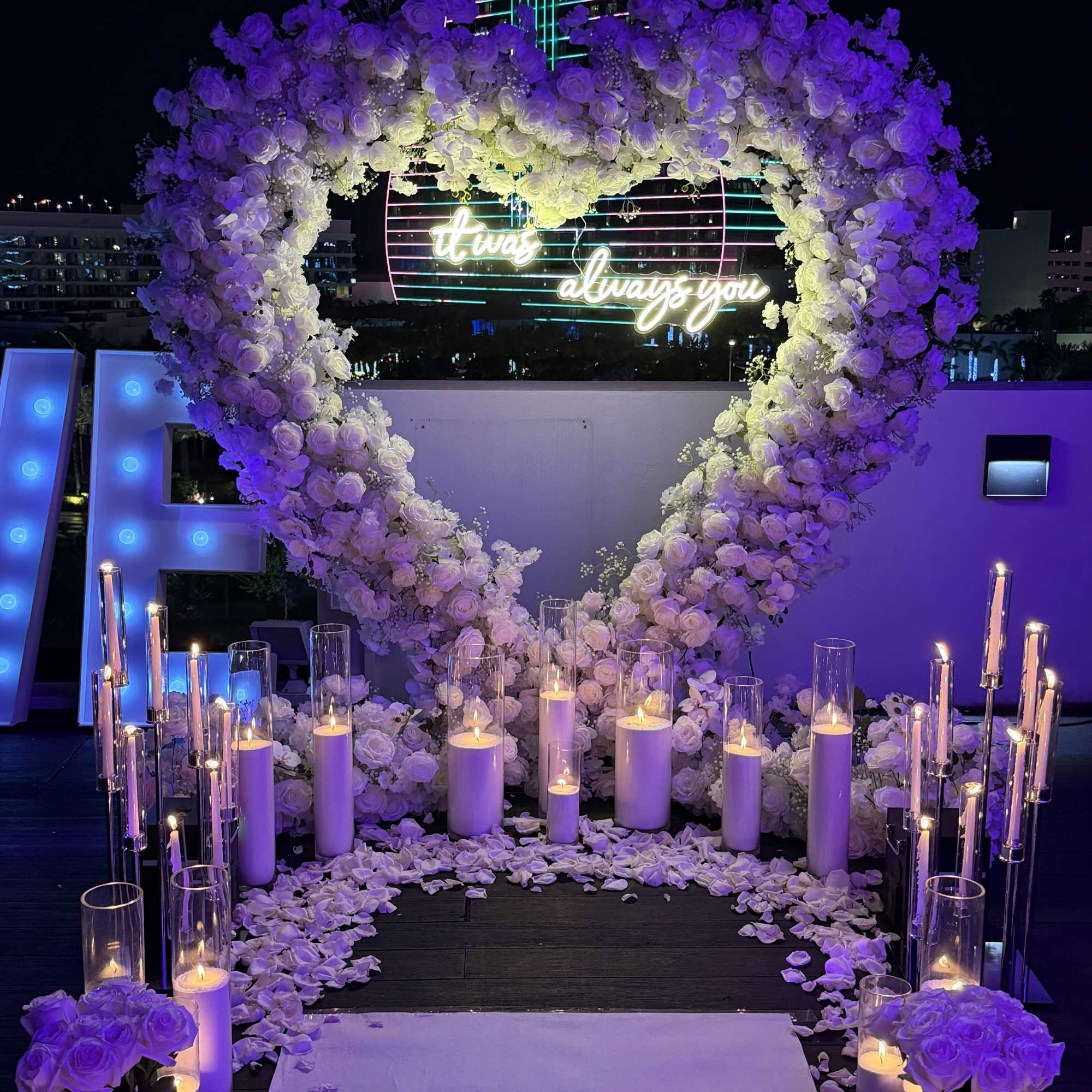 Heart-shaped white rose floral arch with candles and petals at night
