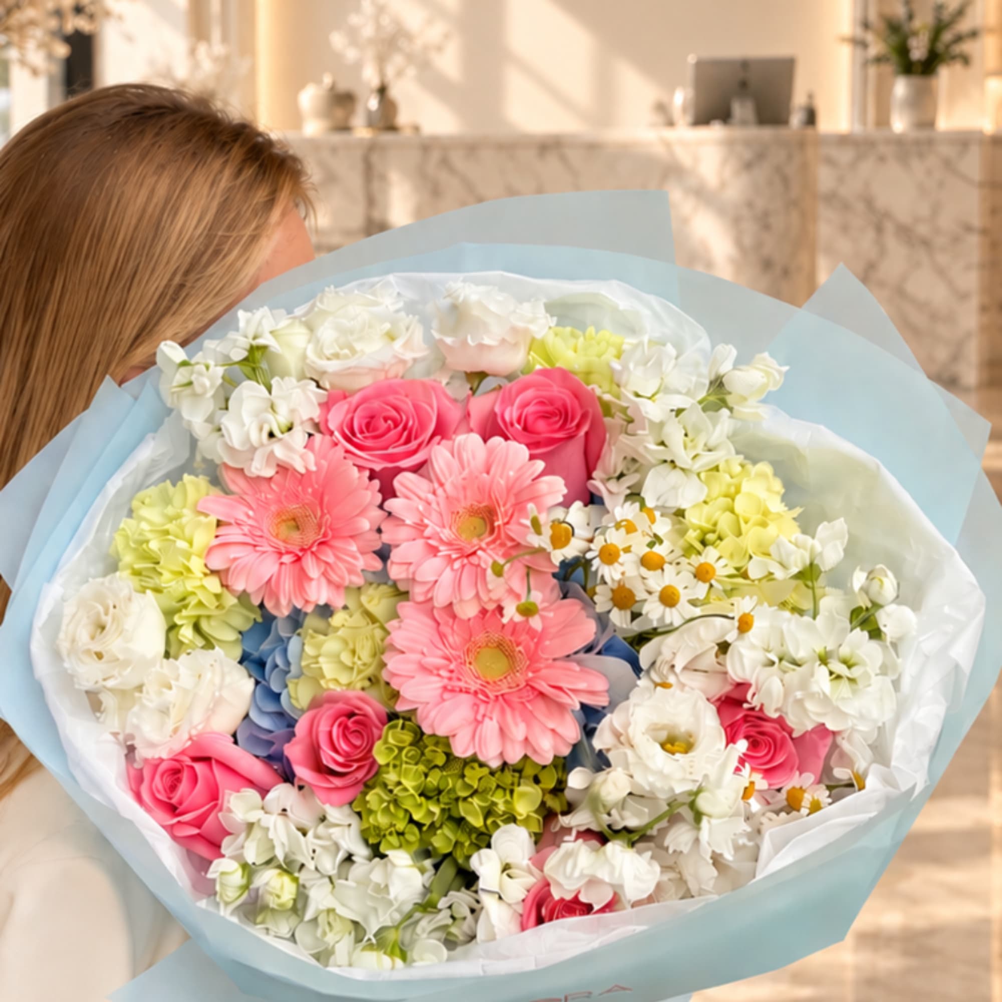 Large pastel bouquet with pink roses, gerbera daisies, and white flowers wrapped in blue paper