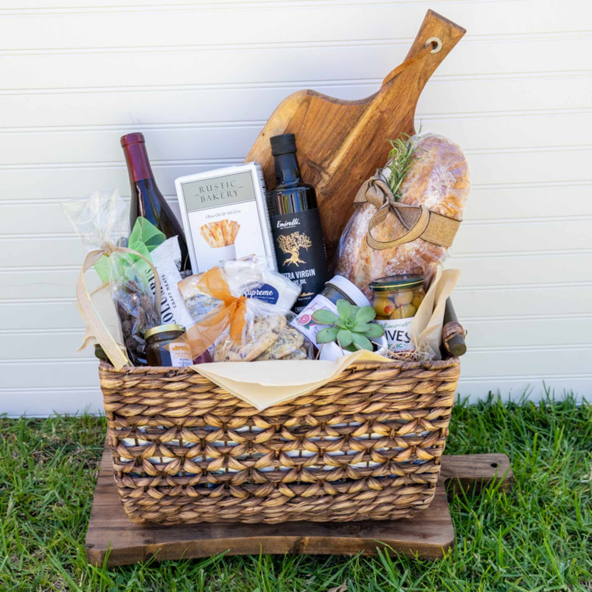 Gourmet gift basket with wine, bread, snacks, and a small succulent in a woven tray.