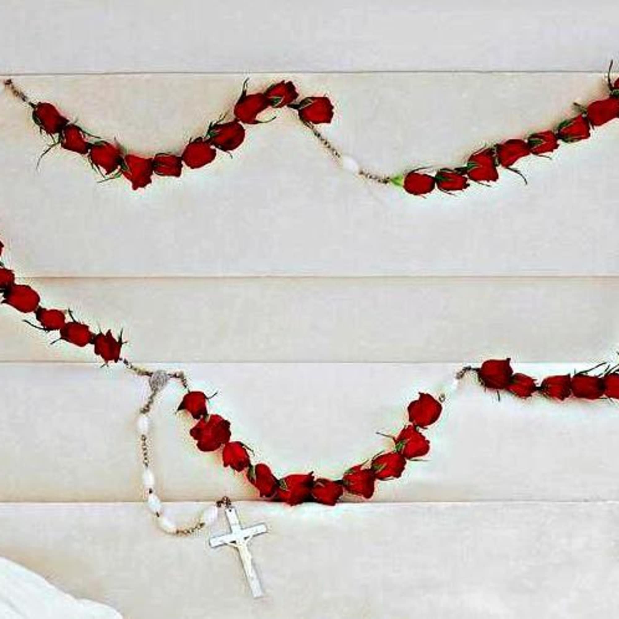 Red rose garland draped across a light upholstered headboard with a white cross necklace