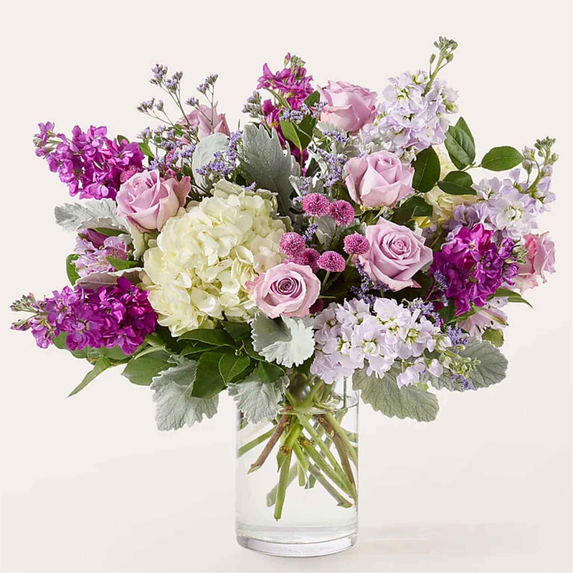 Bouquet of pink roses, hydrangea, and purple flowers in a clear glass vase