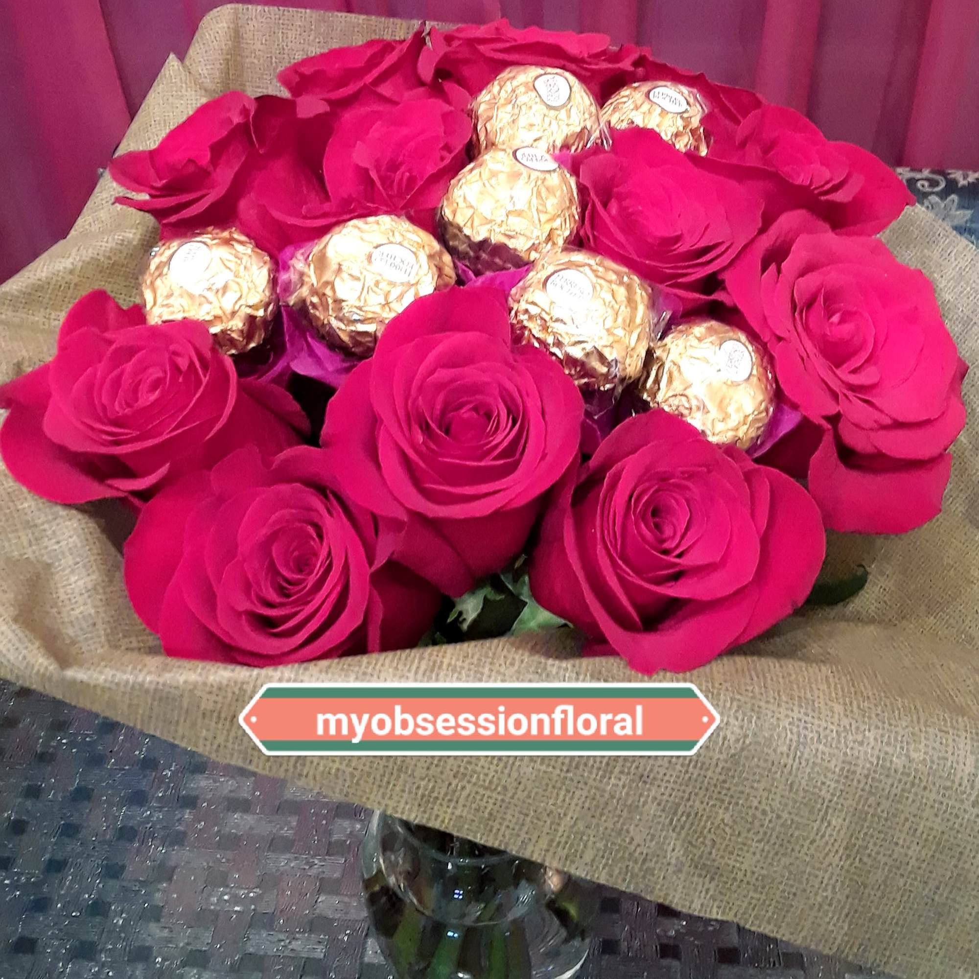 Hot pink roses arranged with gold-wrapped chocolates in a vase.