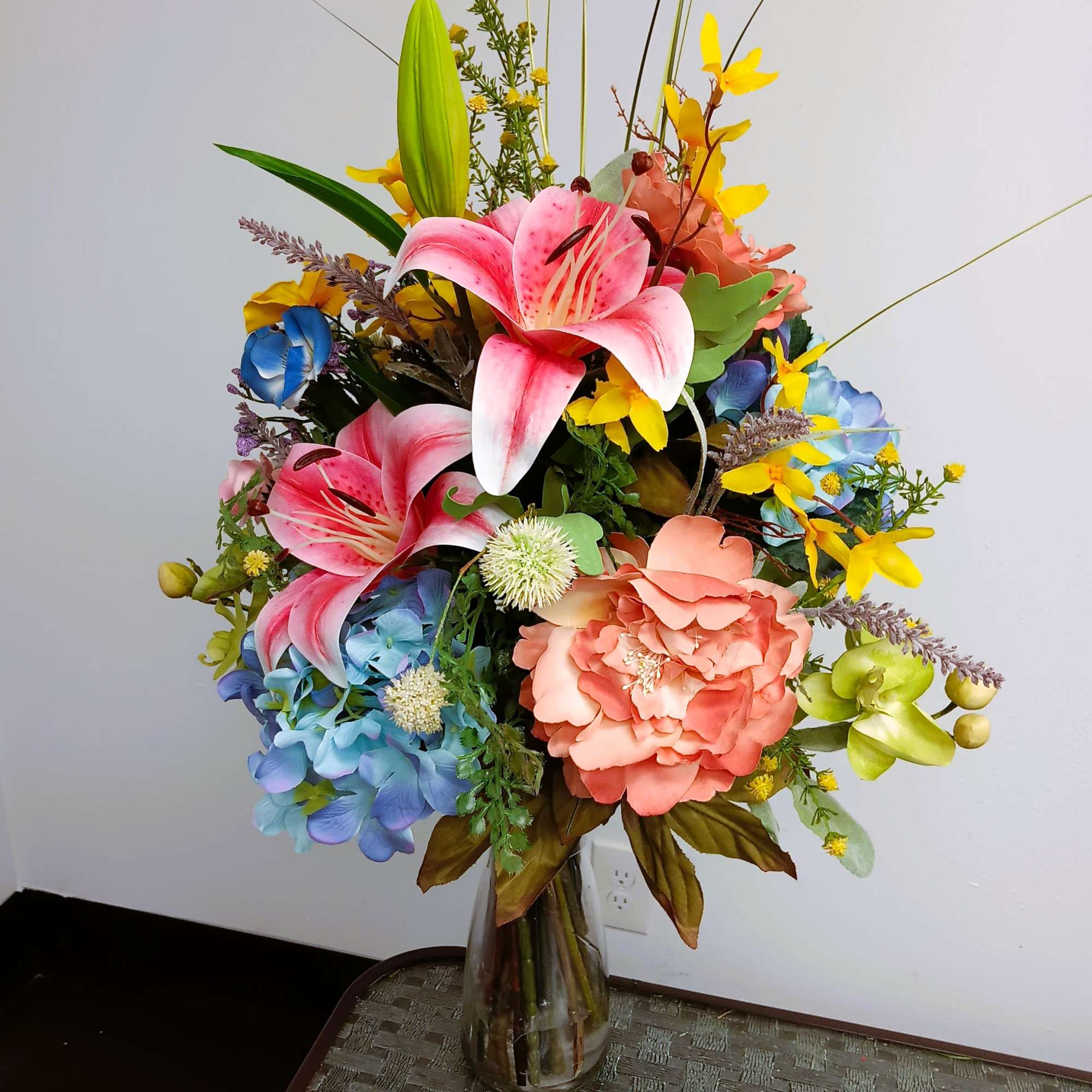 Colorful bouquet of lilies, hydrangeas, and orchids in a glass vase
