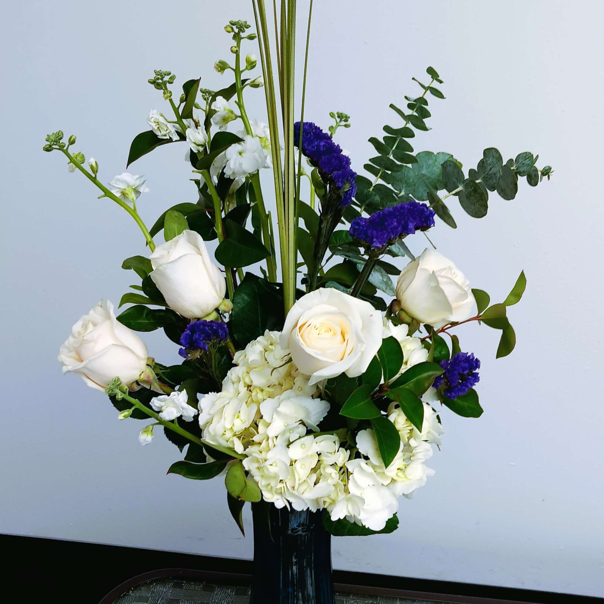 White roses and hydrangeas in a blue vase with purple accents