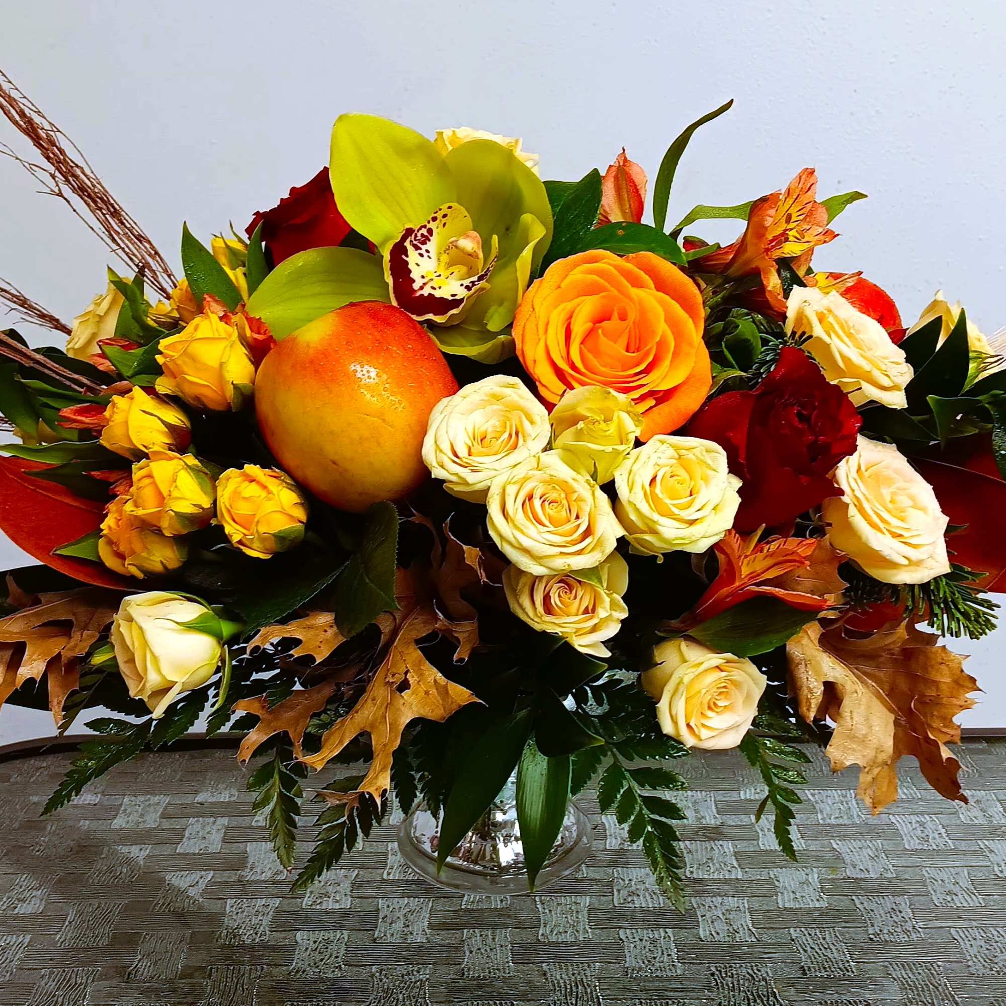 Autumn bouquet with roses, orchids, and an orange fruit in a glass vase