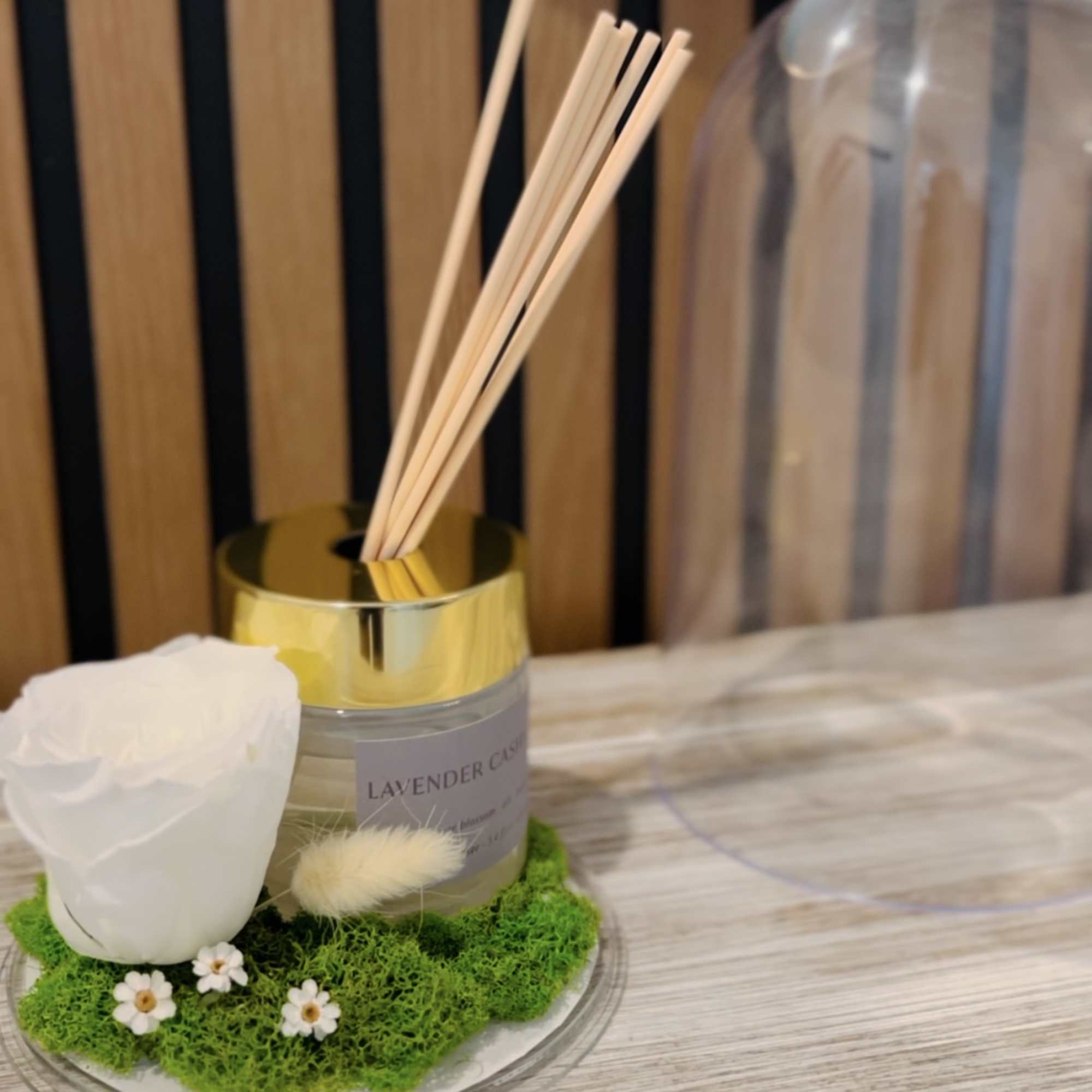 A reed diffuser with a white flower accent on a mossy base