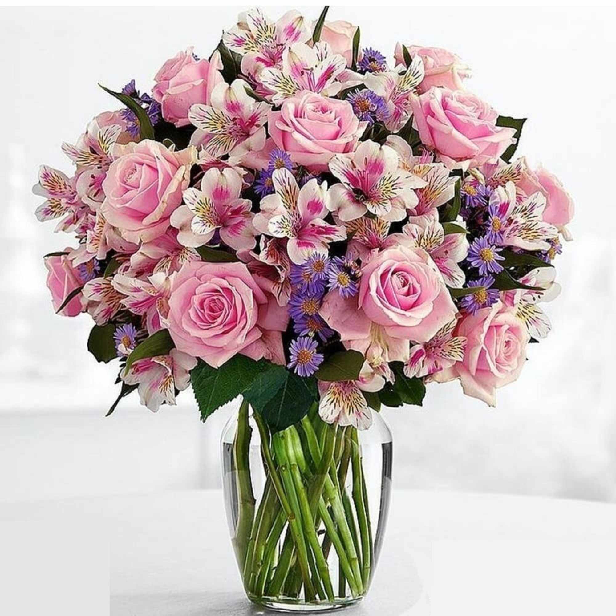 Pink roses and mixed white-purple flowers in a clear glass vase