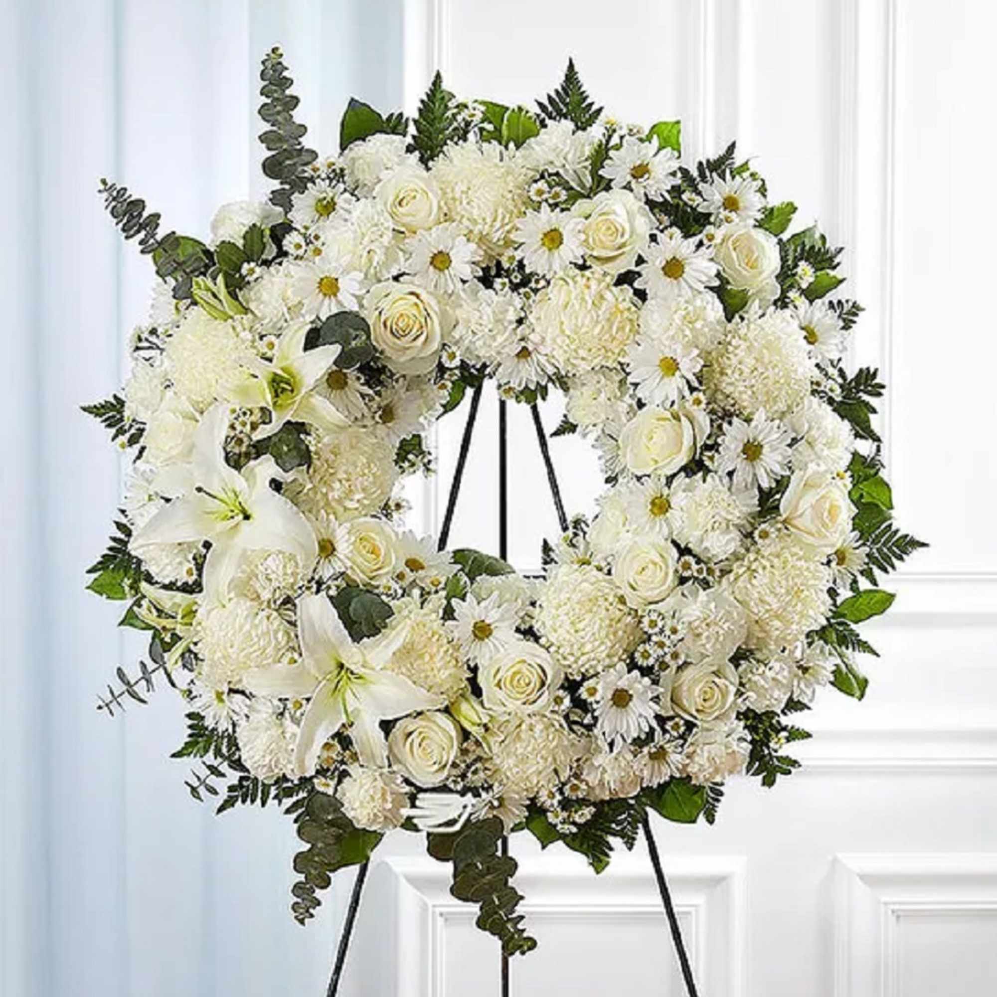 White floral wreath on a black easel with lilies and roses