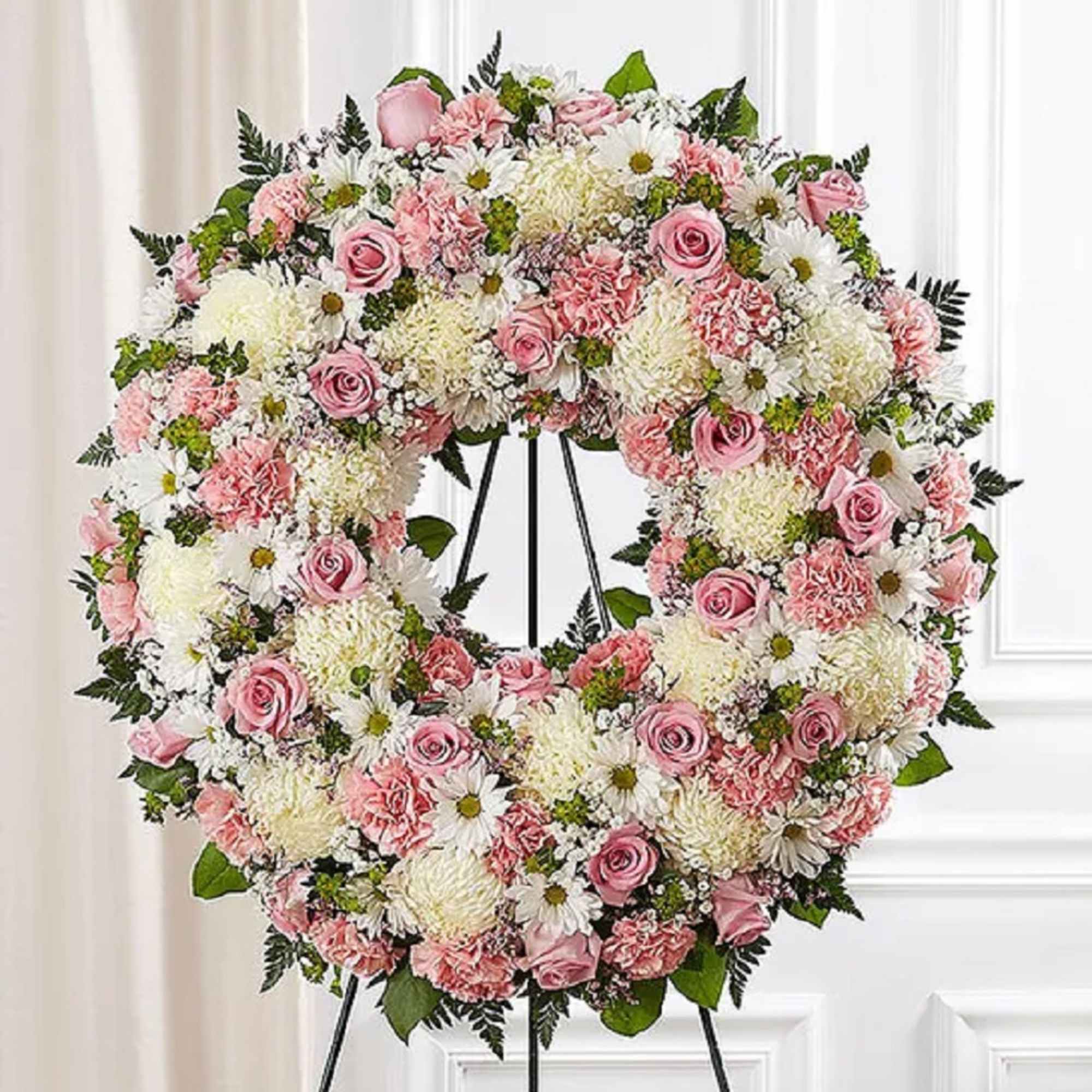 Pink and white floral wreath on a black stand