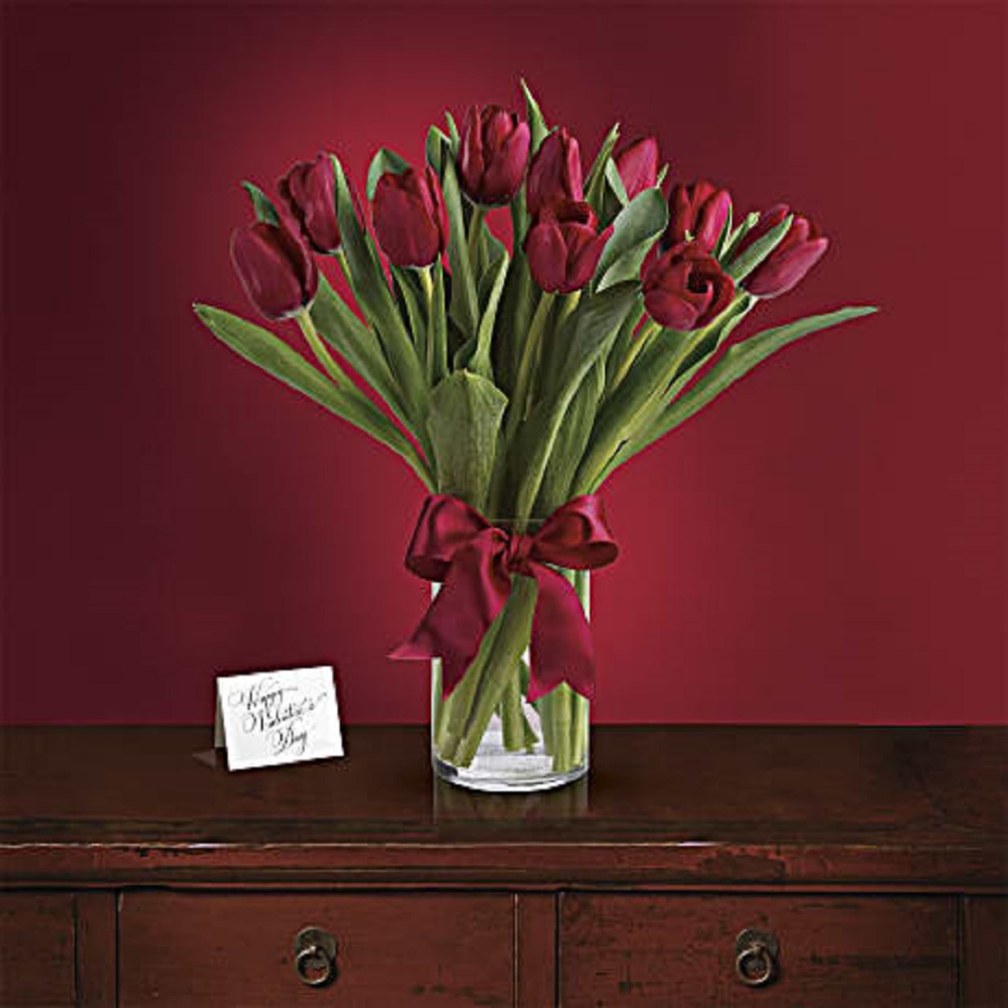 Bouquet of deep red tulips in a clear glass vase with a ribbon