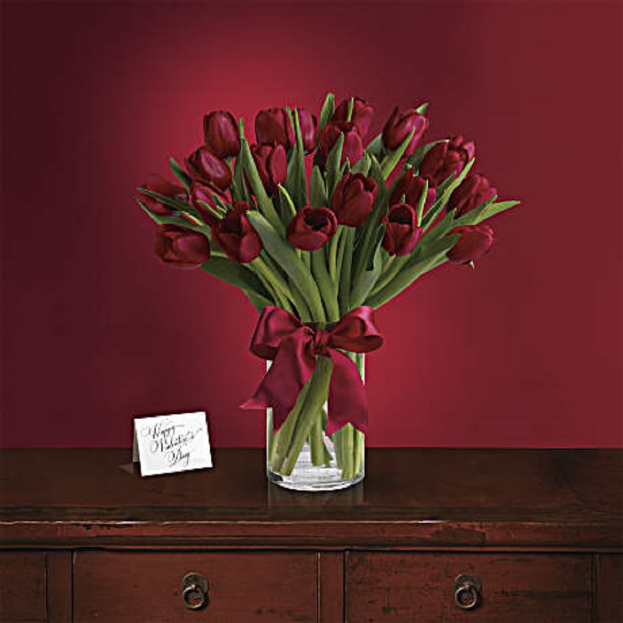 Bouquet of deep red tulips in a clear glass vase with a ribbon