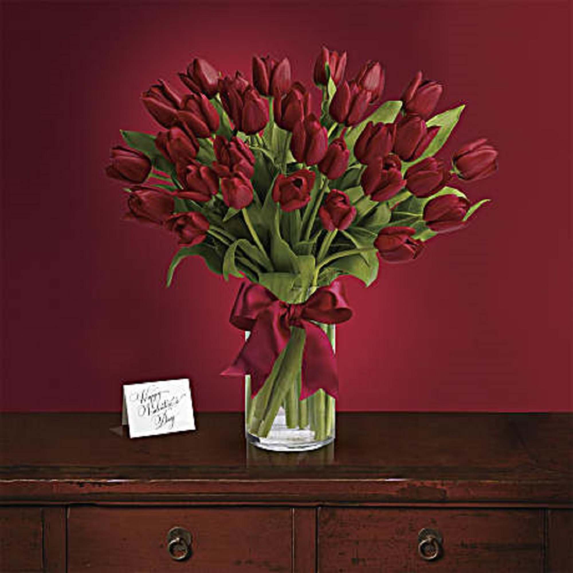 Bouquet of deep red tulips in a clear glass vase with a ribbon