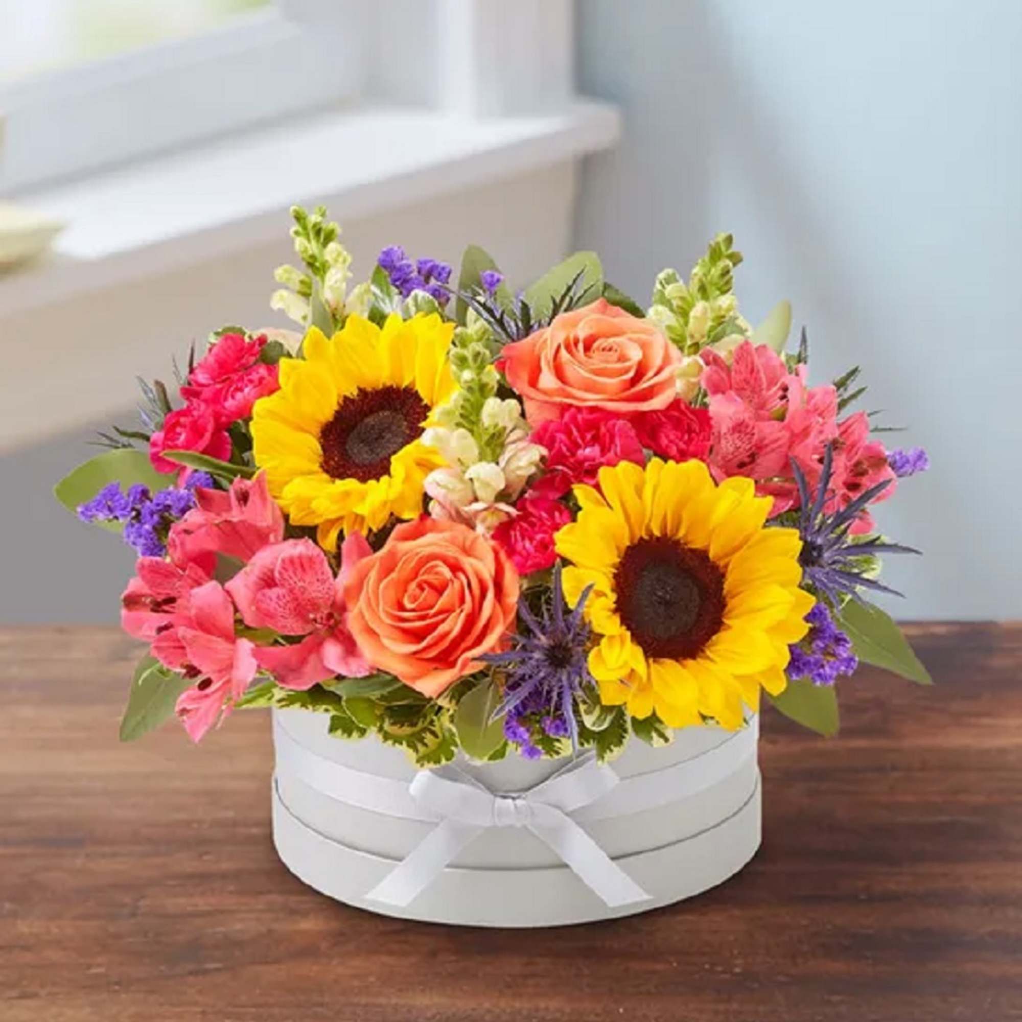 Bright mixed flower arrangement in a white round box with ribbon