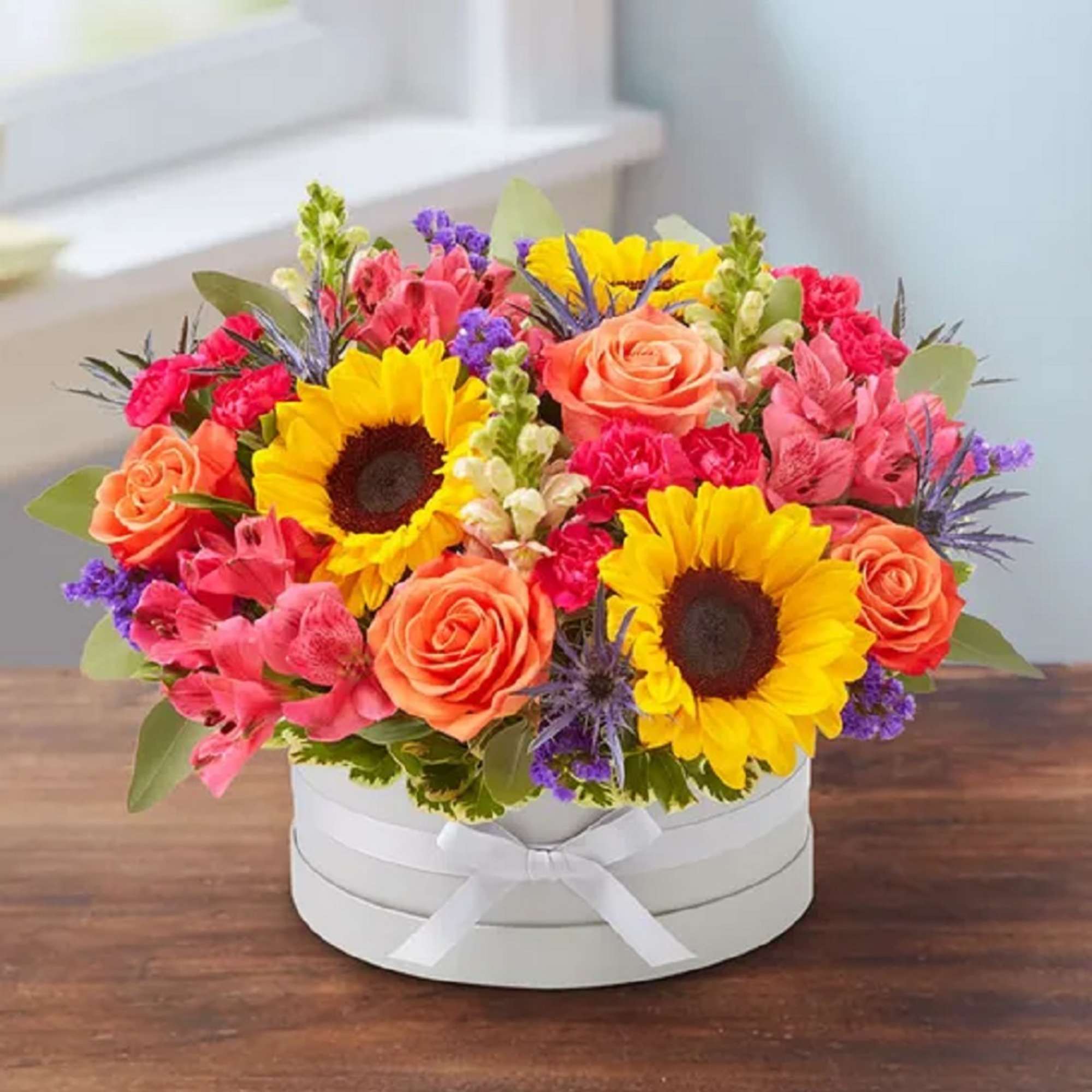 Mixed bouquet with sunflowers, roses, and pink blooms in a white hat box