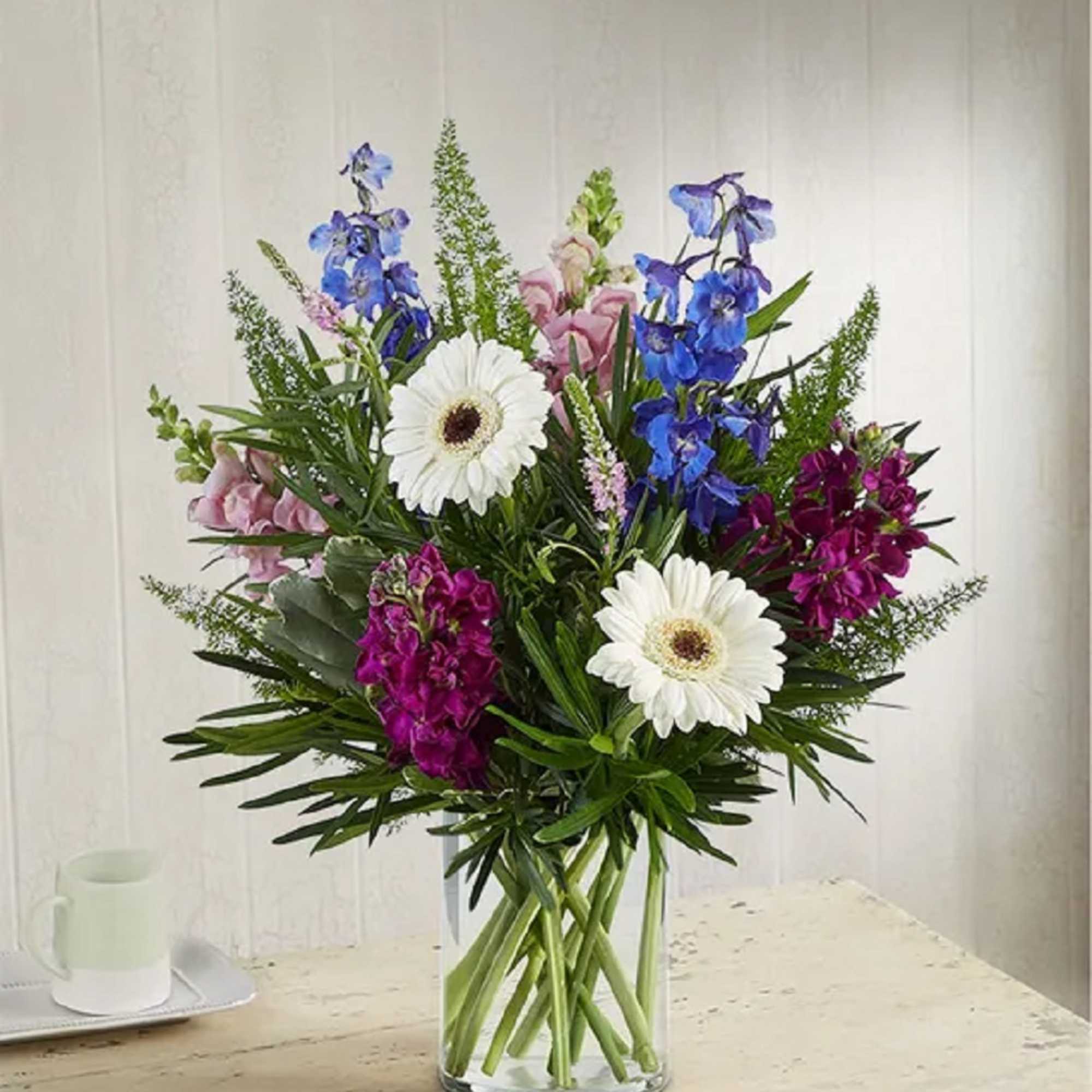 Mixed bouquet with white daisies, blue and pink flowers in a clear glass vase