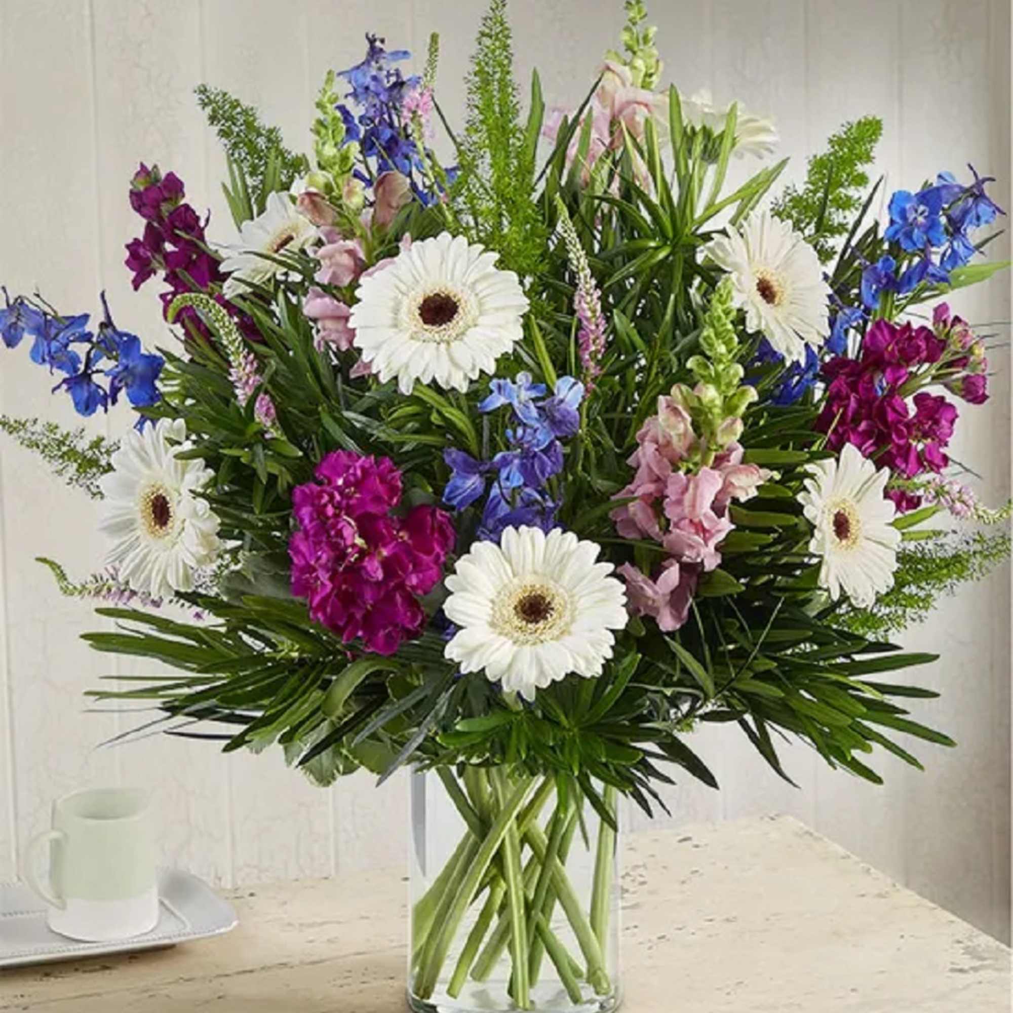 Mixed bouquet with white gerbera daisies, blue and pink flowers in a glass vase