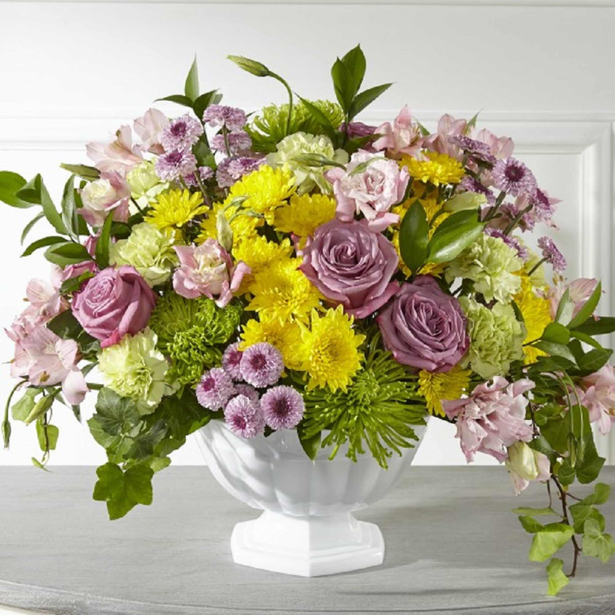 Mixed pink, yellow, and green flower arrangement in a white pedestal vase