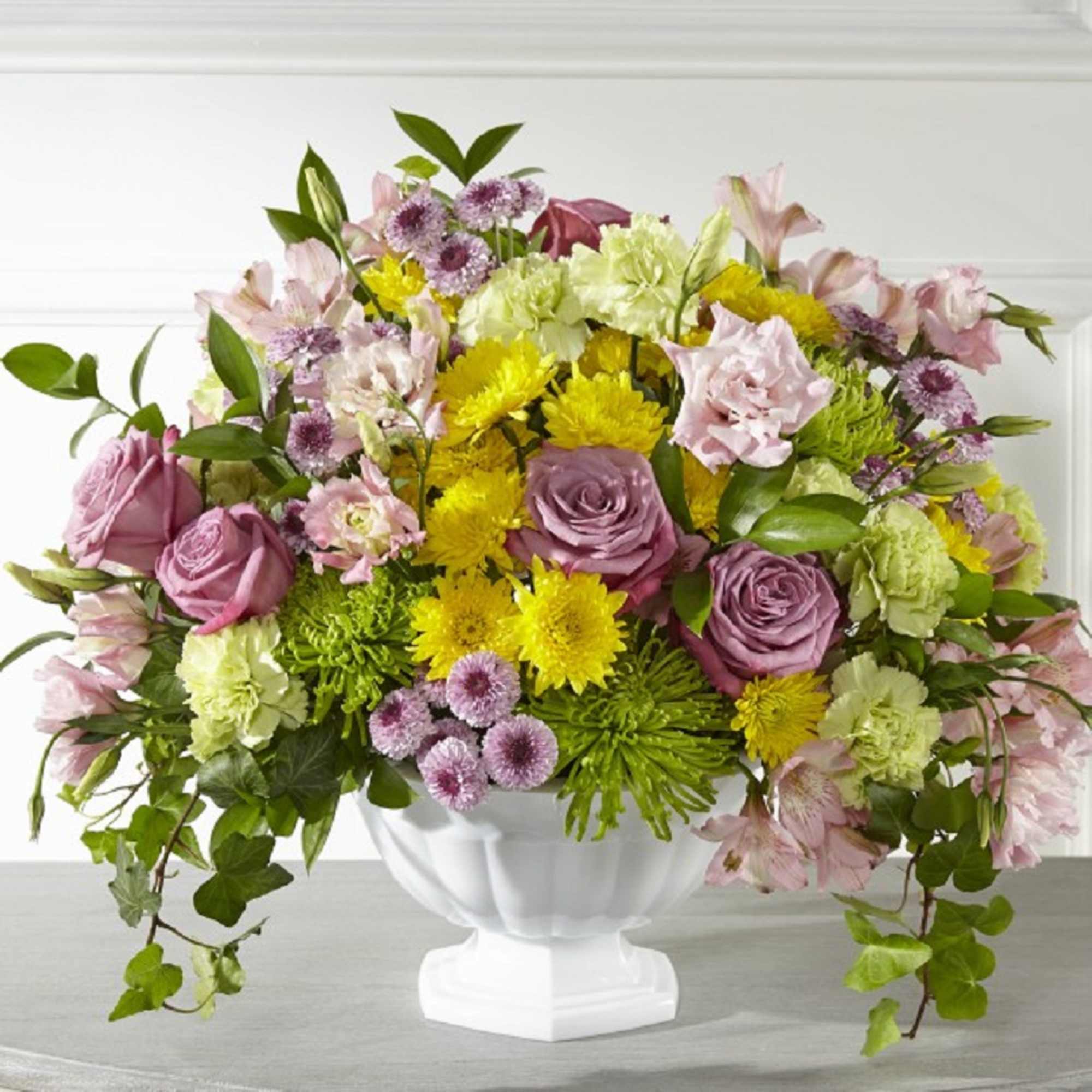 Mixed pink, yellow, and green flower arrangement in a white pedestal vase