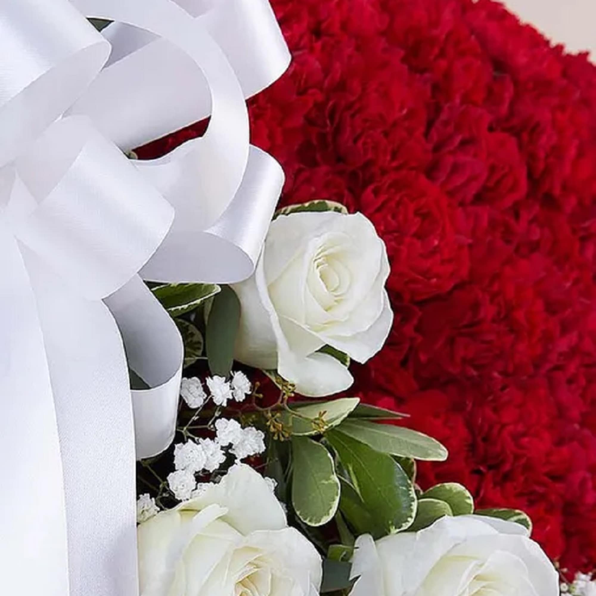 White roses with a large white ribbon against a red carnation background