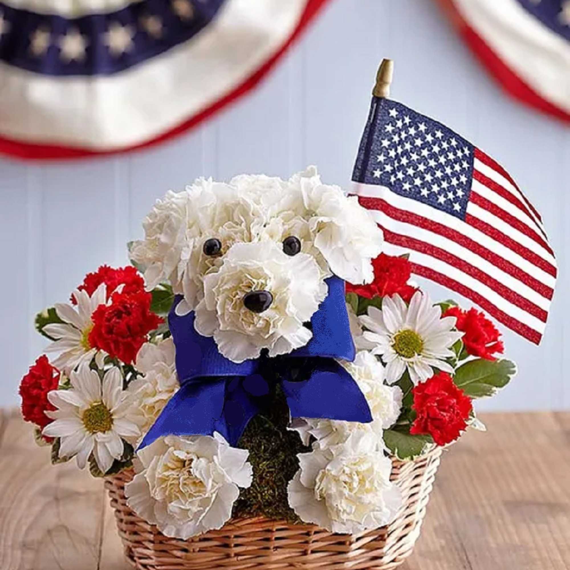 White and red flowers arranged in a basket with a small American flag and blue ribbon.