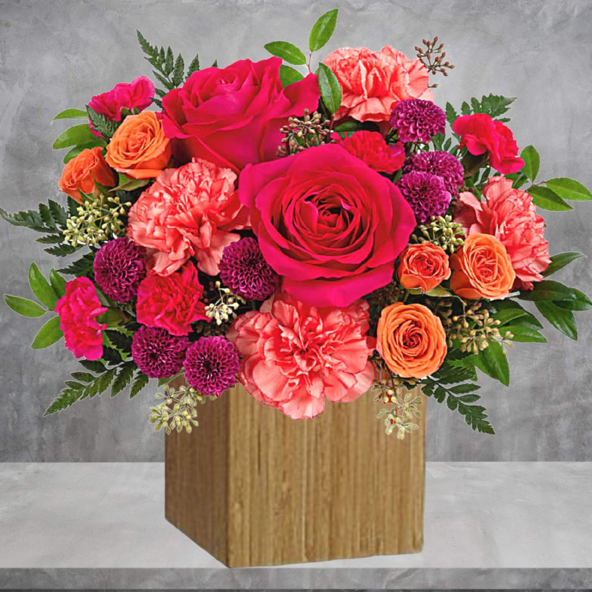 Bright mixed bouquet in a wooden cube vase with pink, orange, and purple blooms